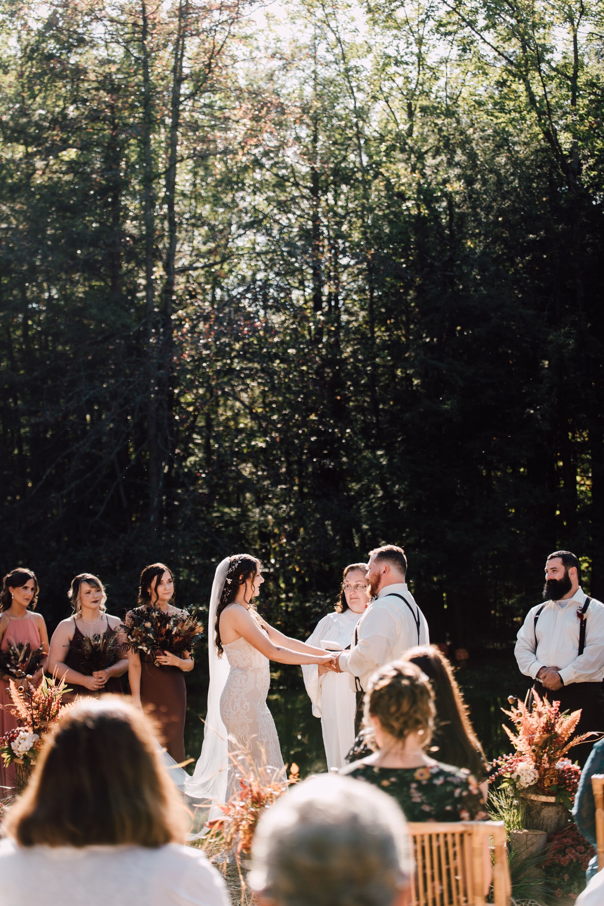  The bride and groom stand together holding hands at their outdoor fall wedding ceremony 