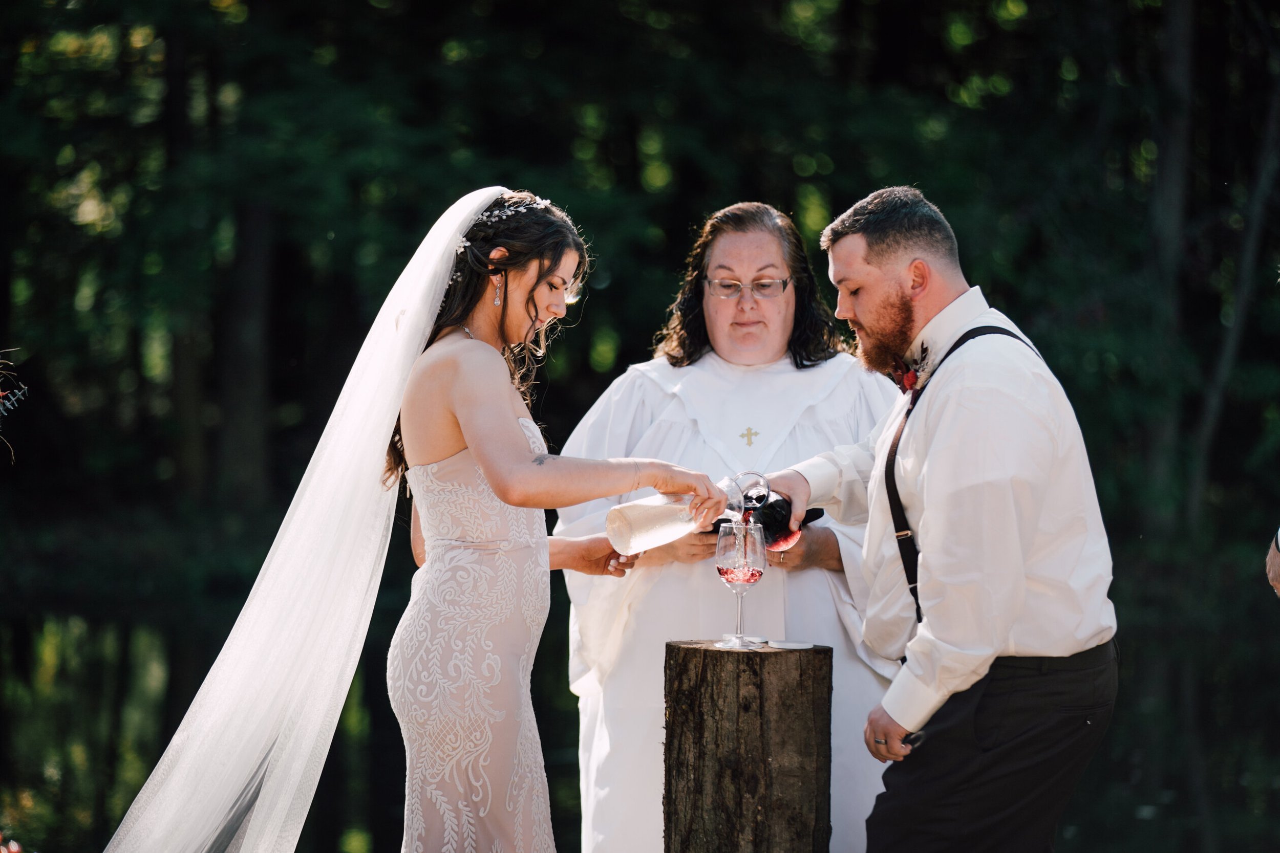 The bride and groom pour white and red wine into a glass during their wine unity ceremony 