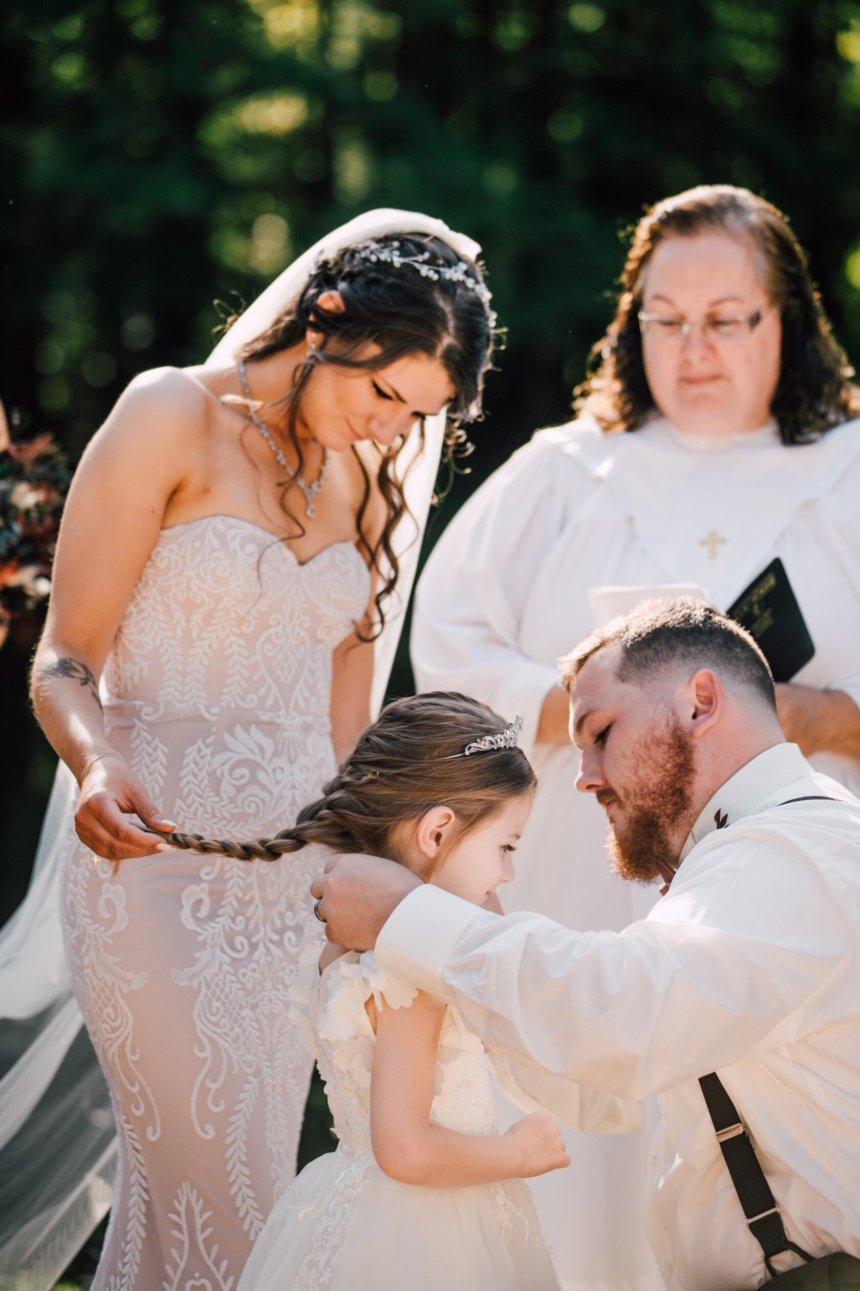  The bride holds her daughter’s hair back as her now husband puts a necklace on her at their backyard wedding   