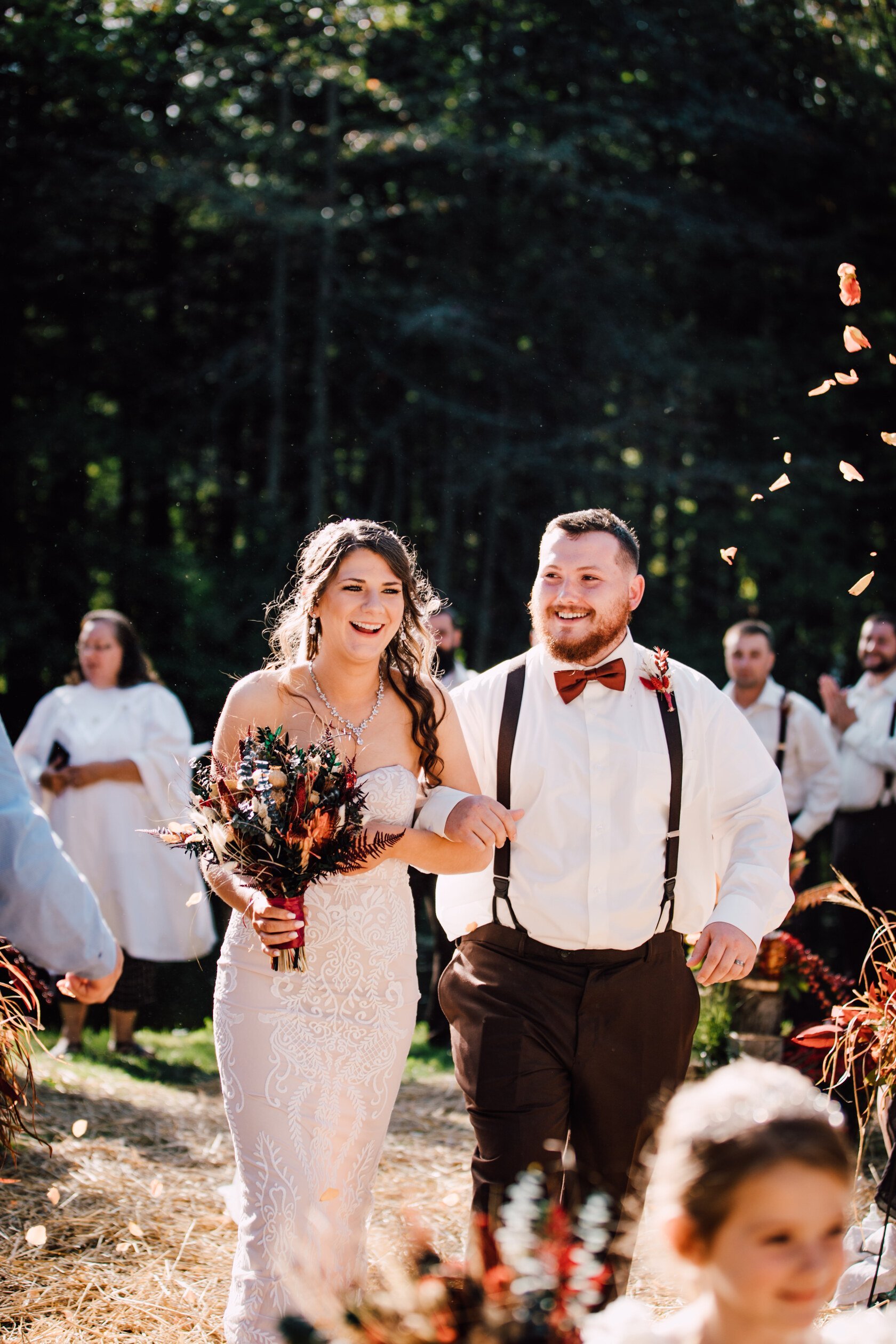  the bride and groom walk down the aisle after their daughter after their outdoor fall wedding 