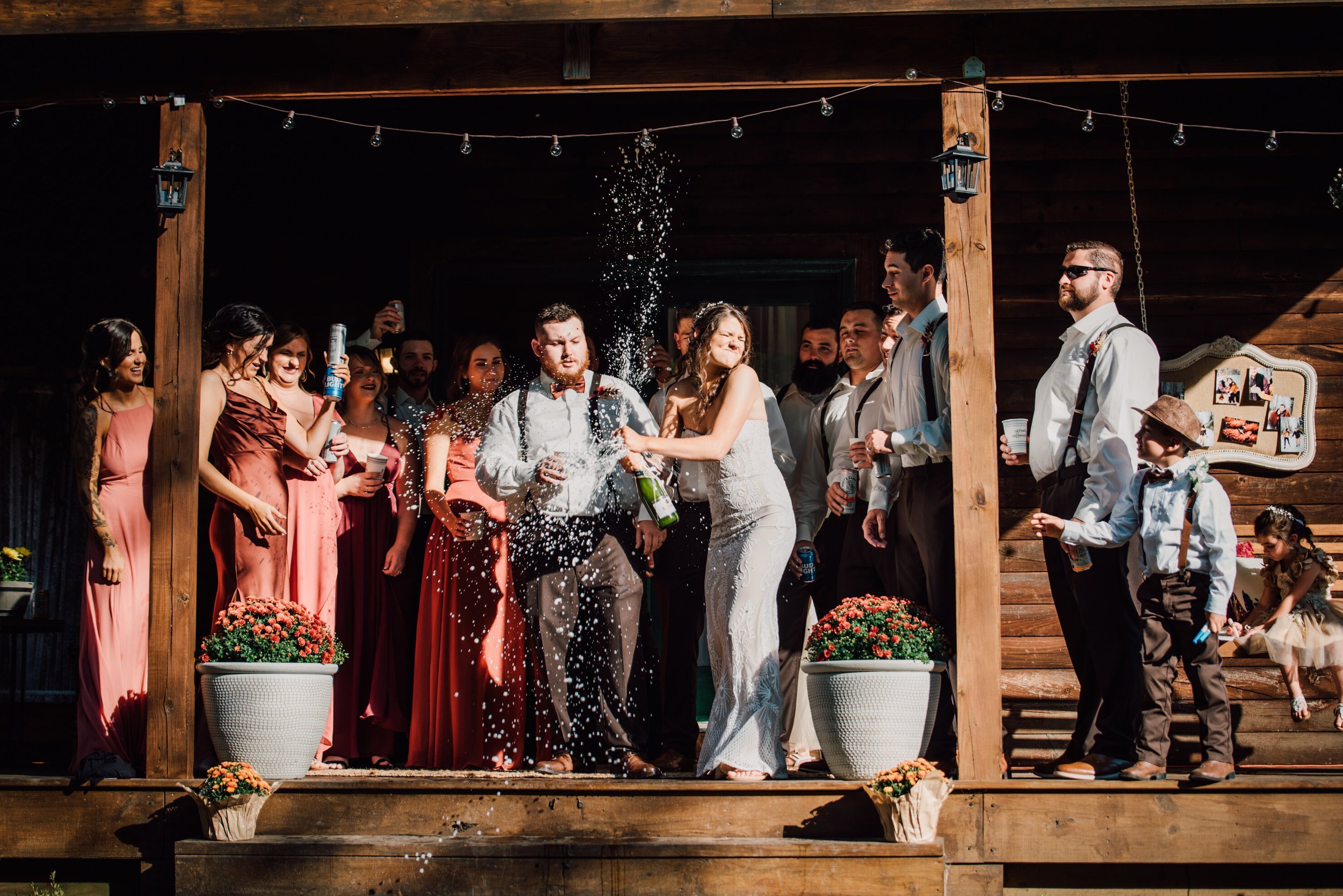  The bride pops a bottle of champagne surrounded by her wedding party after their rustic wedding ceremony 