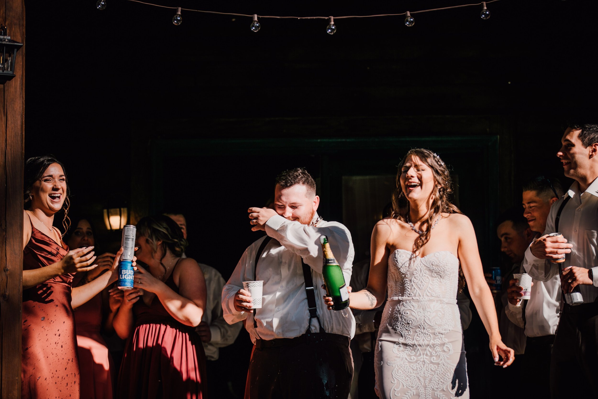  The bride, groom, and wedding party laugh after the bride popped a bottle of champagne after their rustic wedding ceremony&nbsp; 