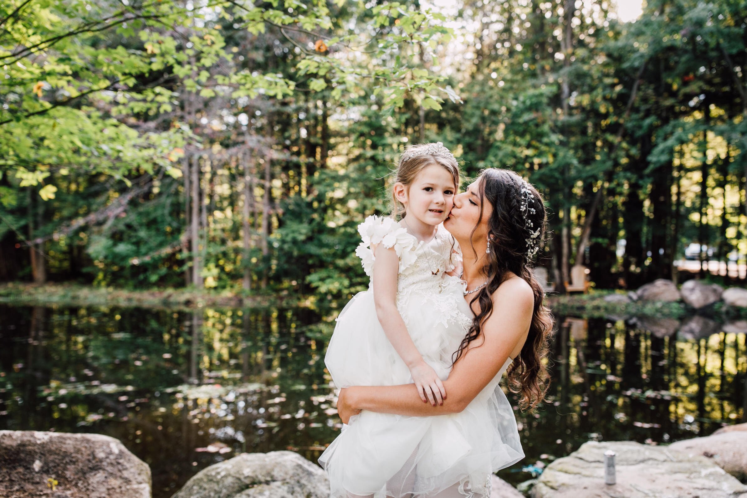  The bride kisses her daughter’s cheek at her outdoor fall wedding 