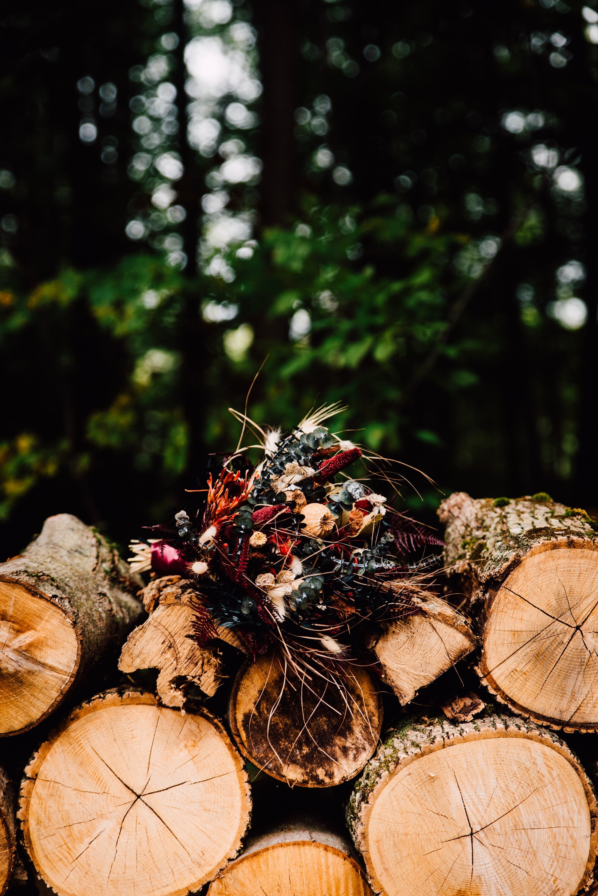  A dried bouquet sits on top of a stack of fire wood 