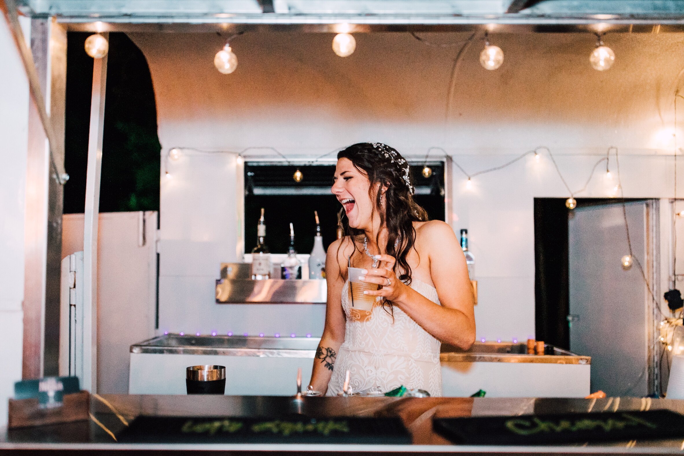  The bride laughs in the mobile bar at her rustic wedding reception 