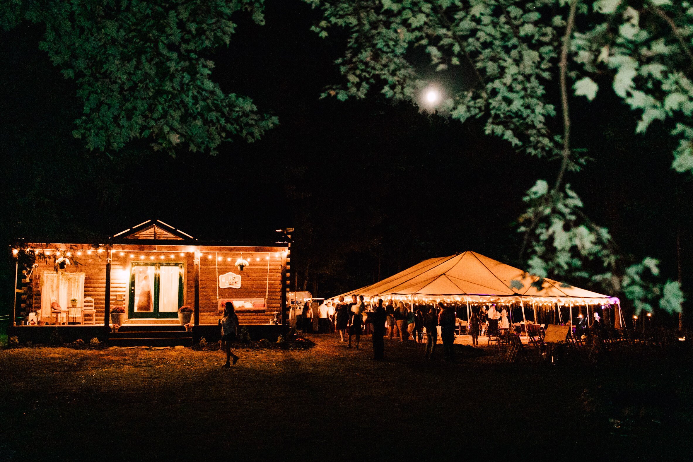  The outdoor fall wedding venue is pictured lit up at night by string lights with guests enjoying the night 