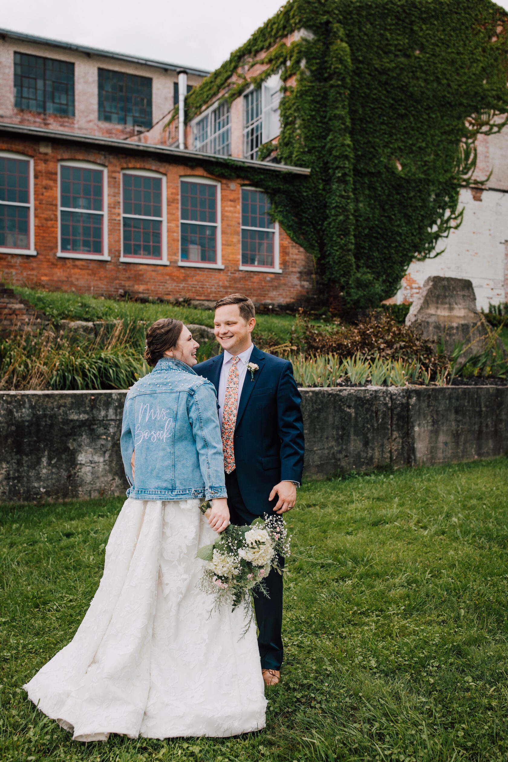  Bride and groom look at each other while the bride wears her custom wedding jean jacket in Geneva ny 