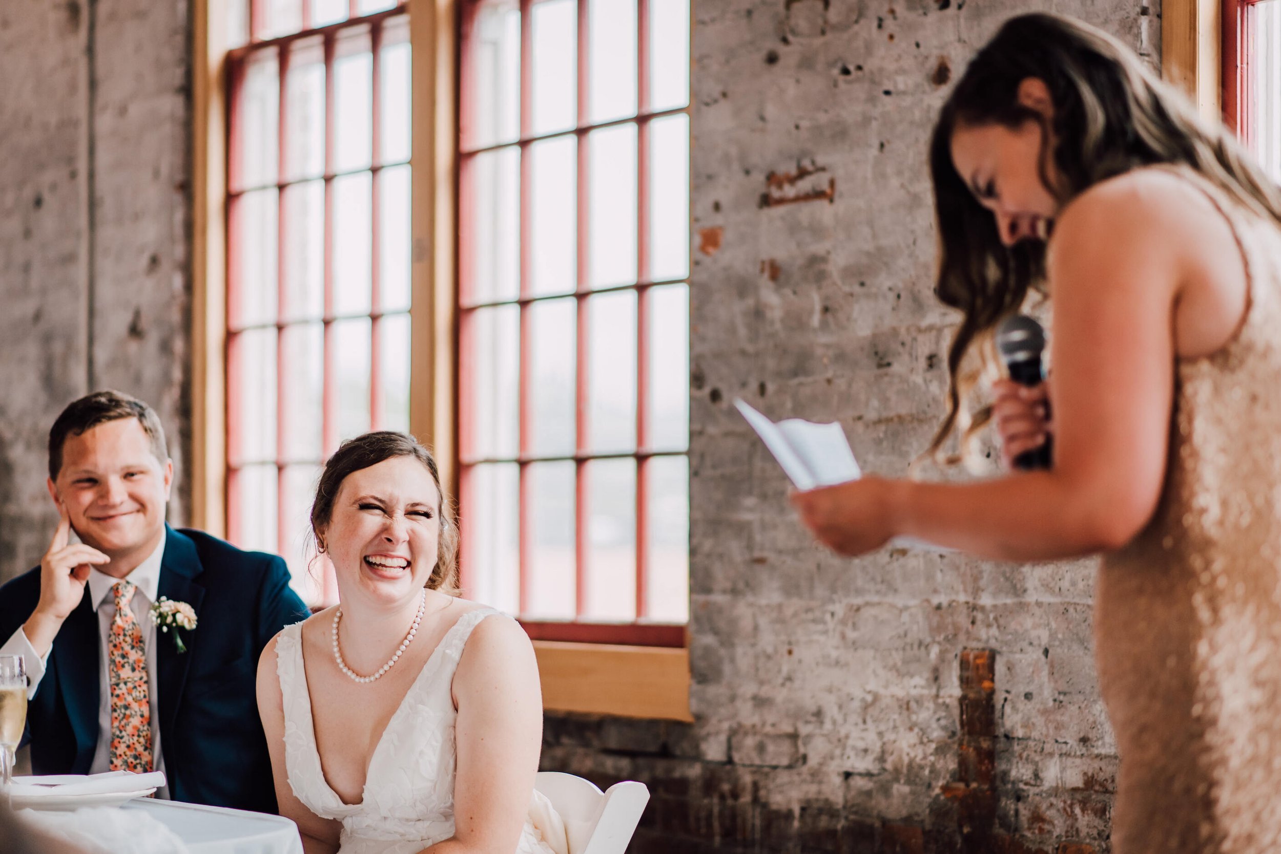 Bride laughs next to her groom during toasts at their warehouse wedding 
