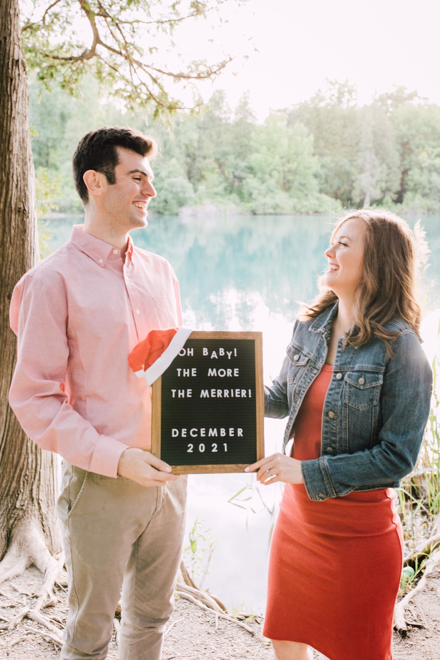  Parents to be smile at each other with their letterboard pregnancy announcement announcing their December baby 