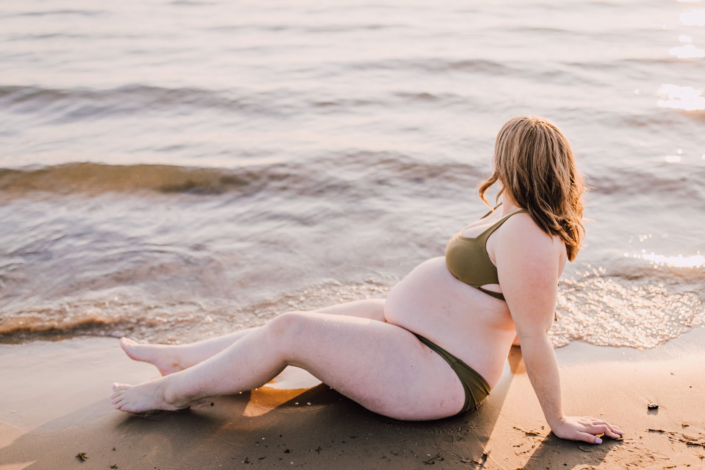  A woman lays on the beach and looks out onto the water, beach maternity photos&nbsp; 