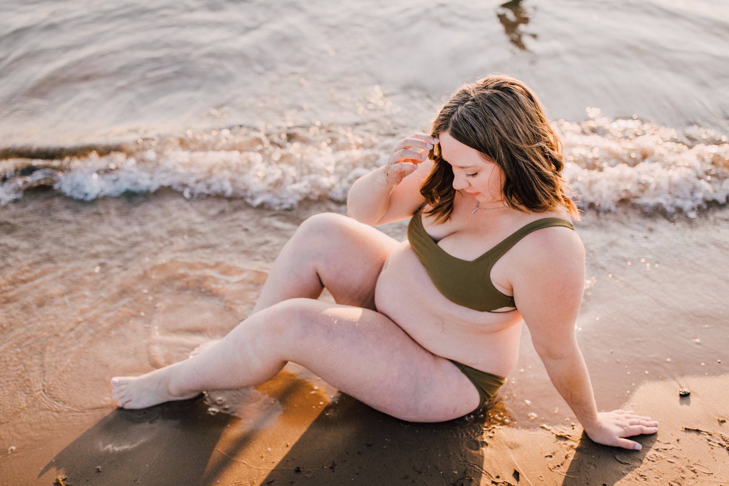  A pregnant mother sits on the beach and looks down, beach maternity photos 