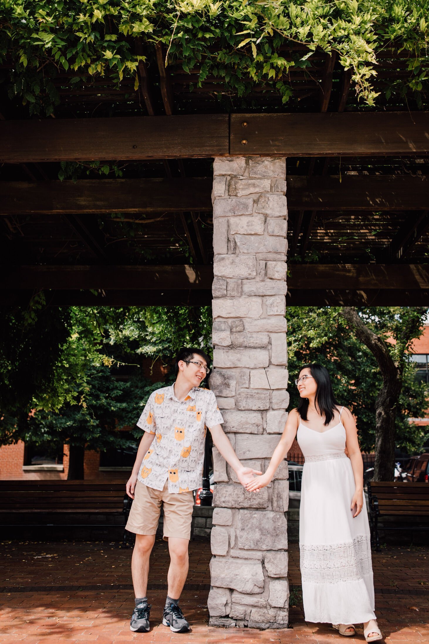  A couple holds hands from either side of a stone pillar, downtown engagement pictures&nbsp; 