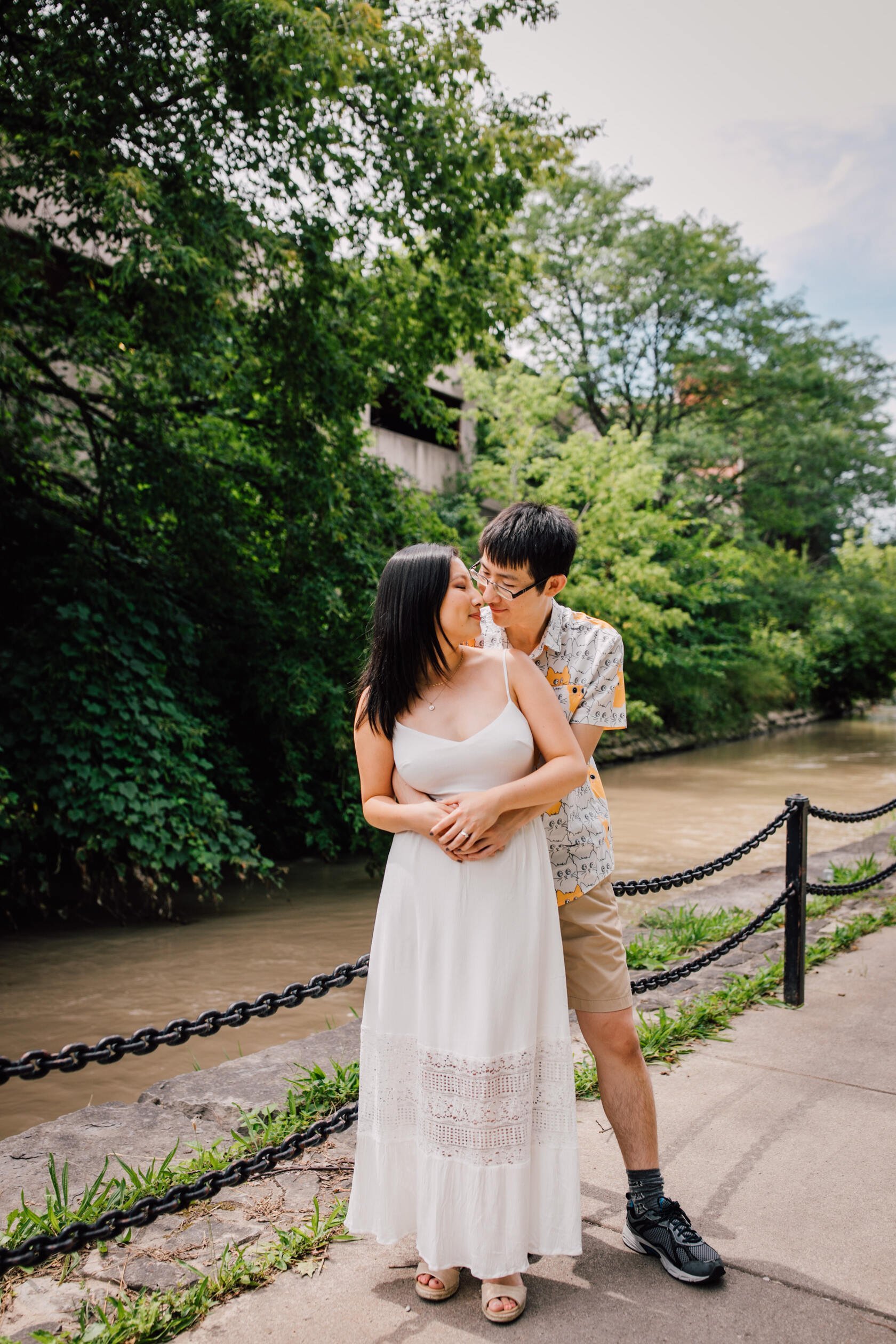  An engaged couple stand together in front of a creek, Syracuse creekwalk&nbsp; 