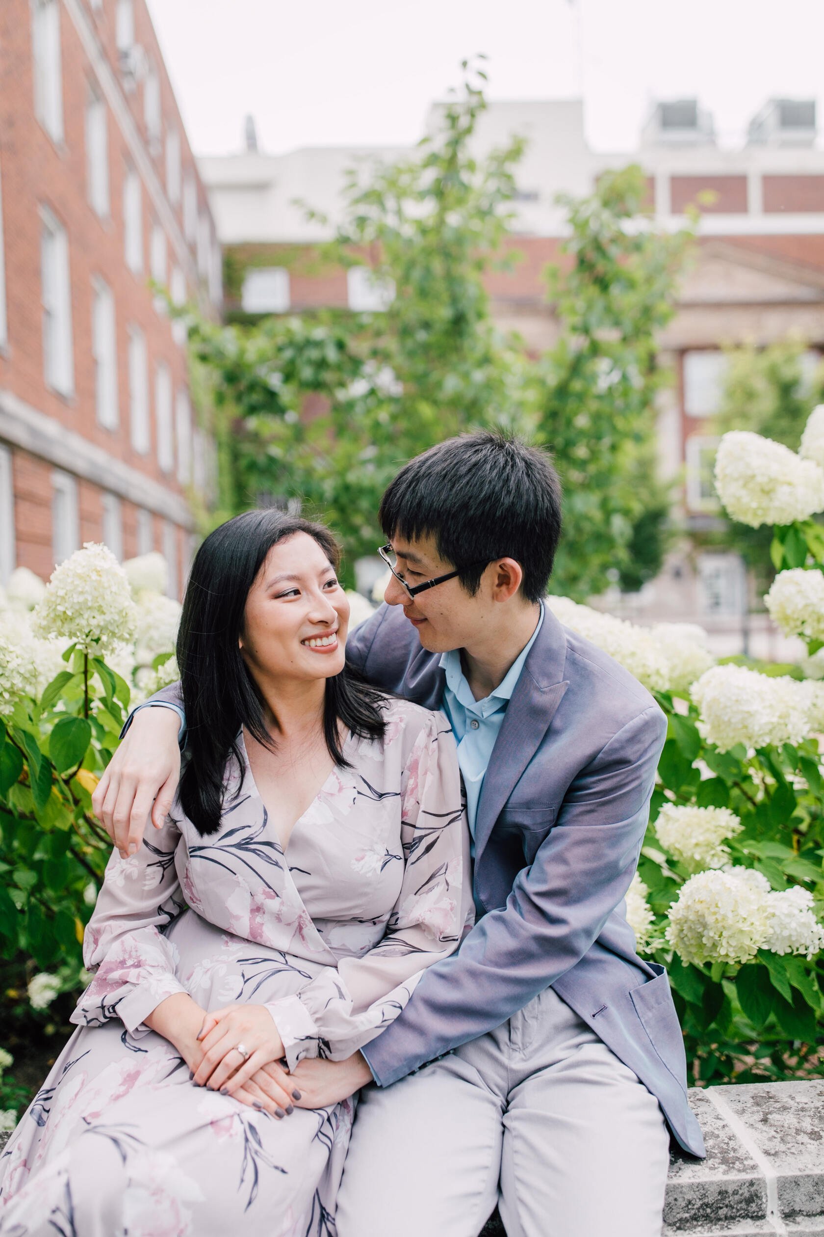  Engaged couple smile at each other in front of hydrangea bushes, engagement photography 