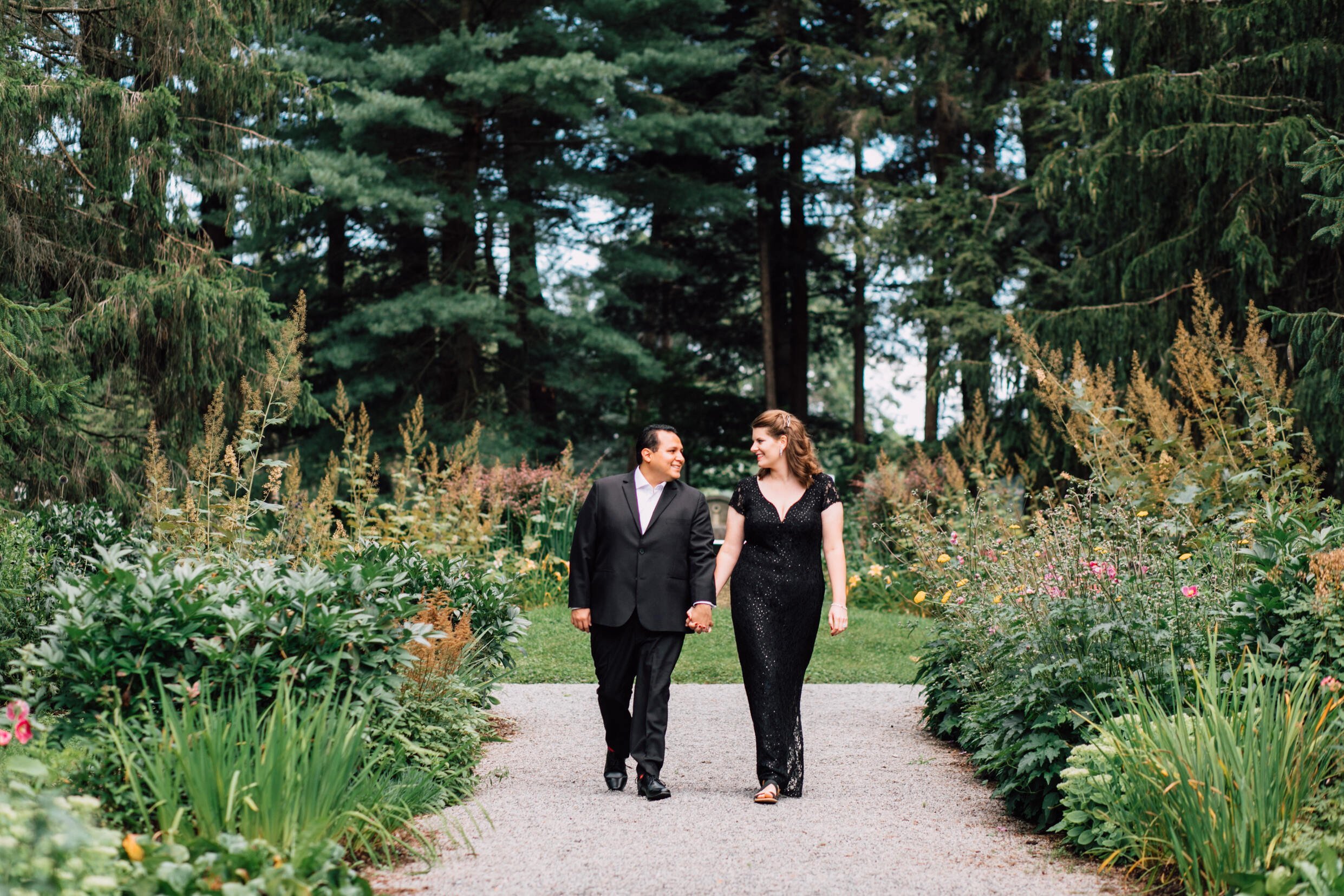  Married couple glance at each other as they walk down a garden path during their anniversary photoshoot 