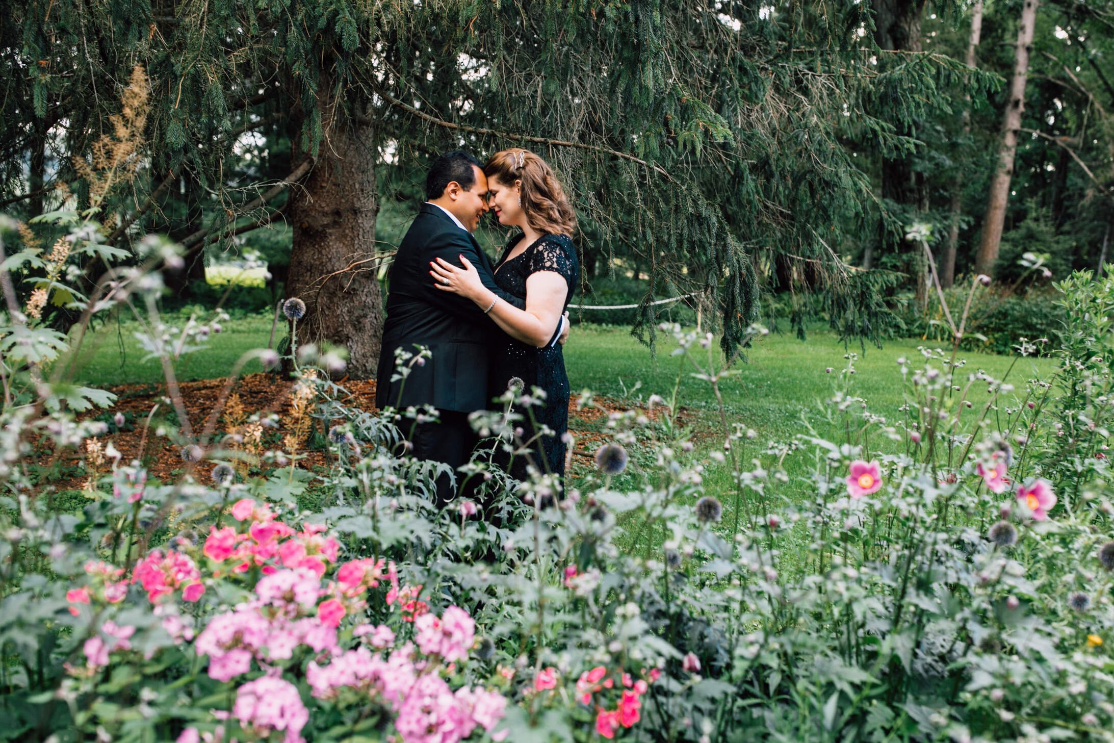  A married couple lean on each other as they stand facing each other in a garden during their anniversary photoshoot in Cazenovia, NY 
