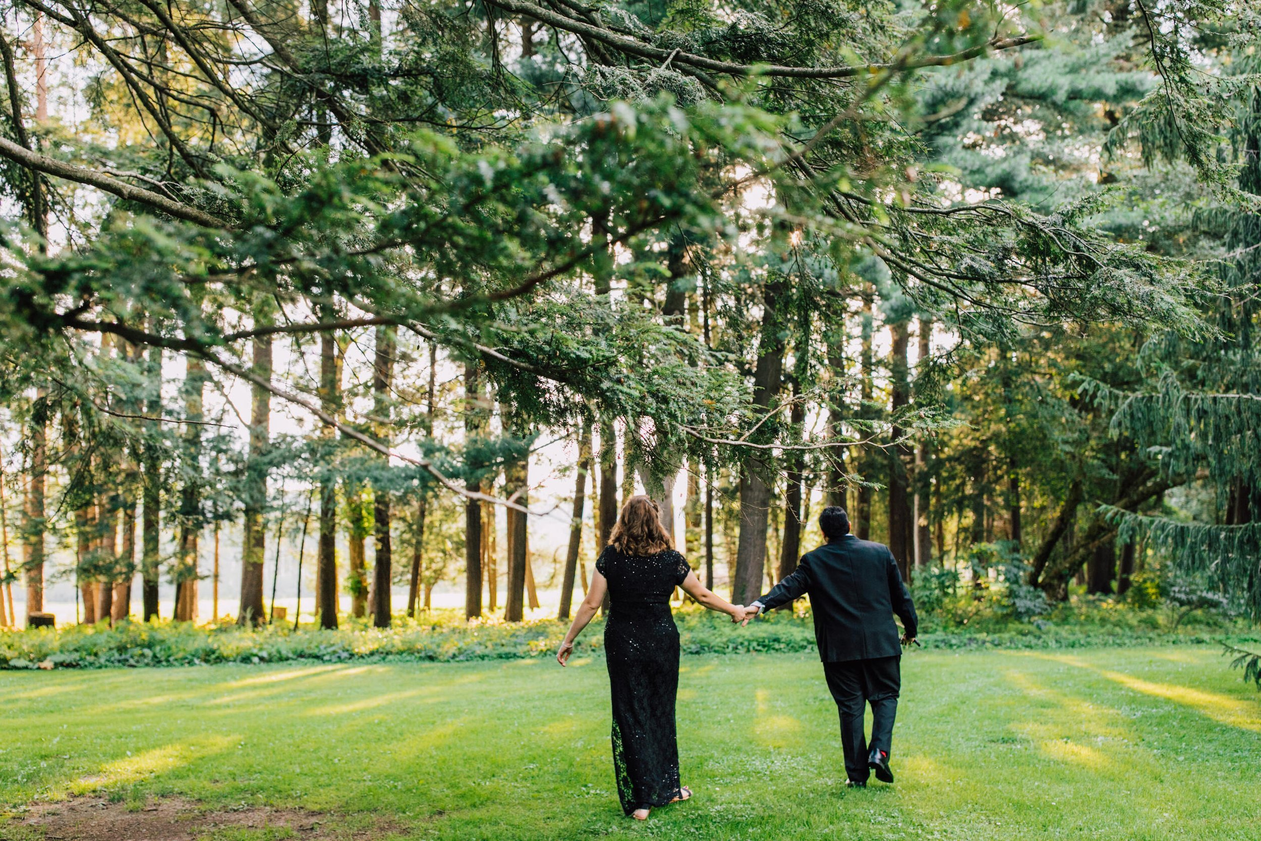  A married couple stand facing woods hand in hand during their anniversary photoshoot 
