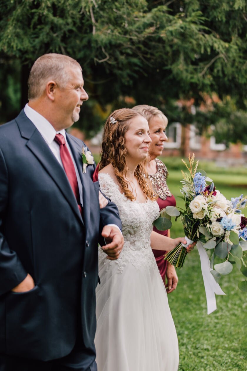  Bride walks down the aisle with her parents at her New York garden wedding 