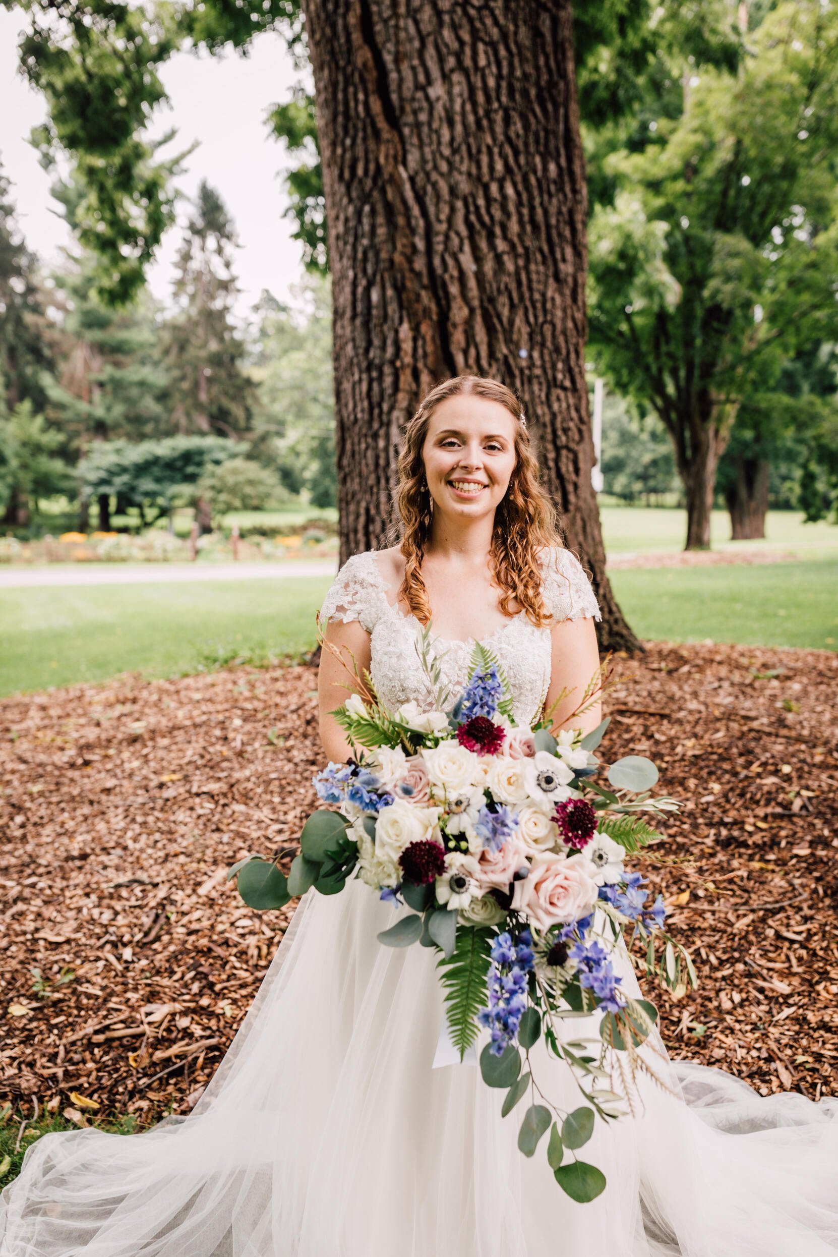  Bride stands smiling with her bouquet during garden wedding photography 