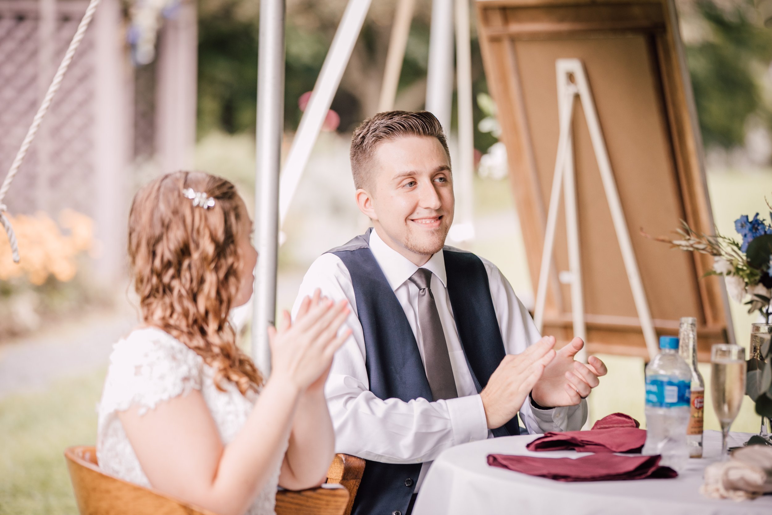  Bride and groom sit listening to toasts at their garden wedding 