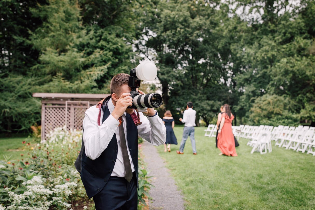  groom takes photographer’s camera and takes photos of his bride after their garden wedding ceremony at oneida community mansion house 