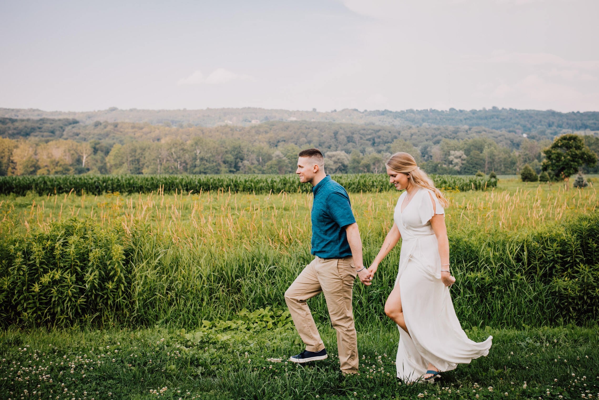  engaged couple walk in front of a roaming field at rocking horse farm while holding hands 