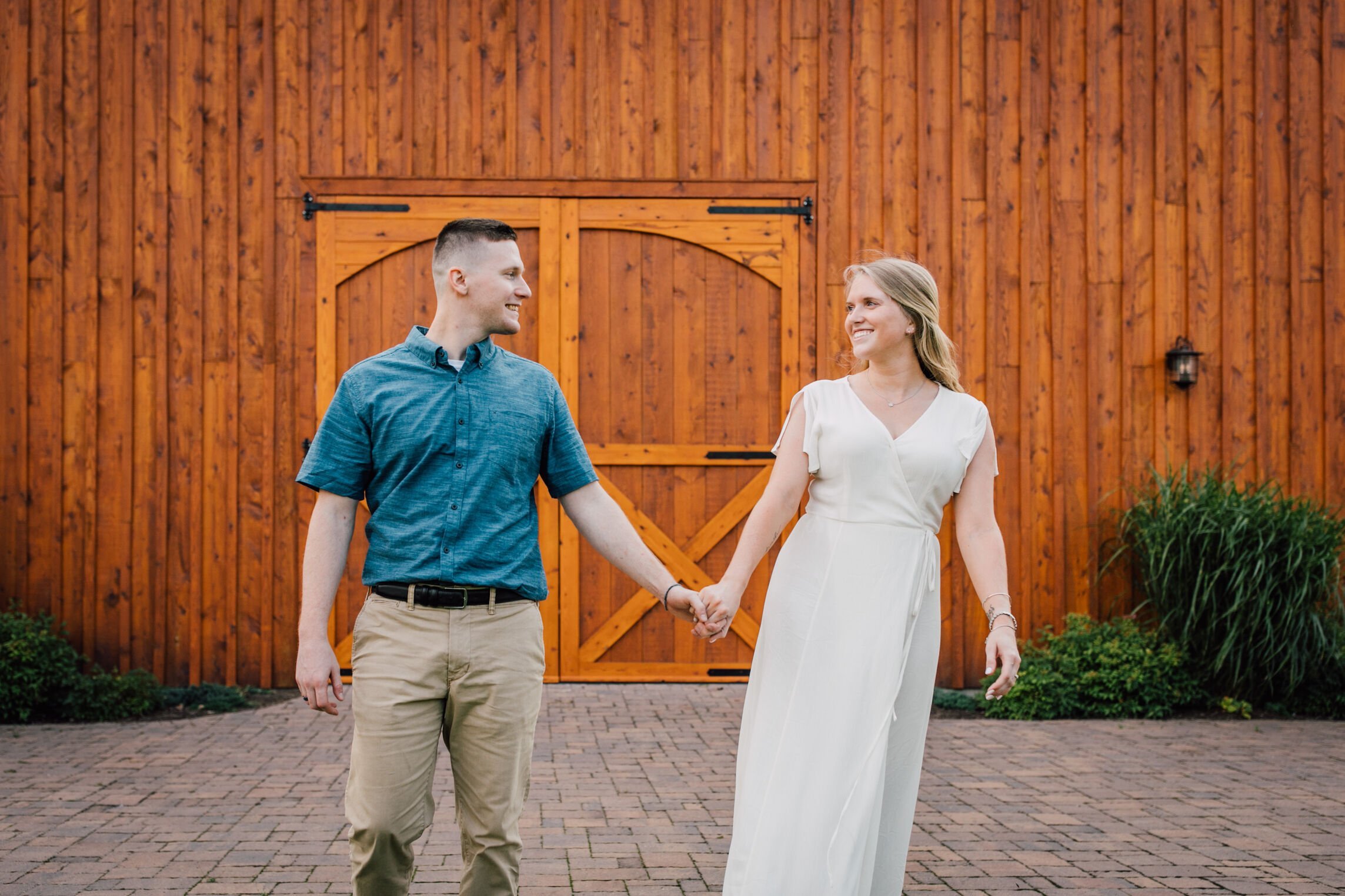  Engaged couple hold hands in front of the barn at rocking horse farm 
