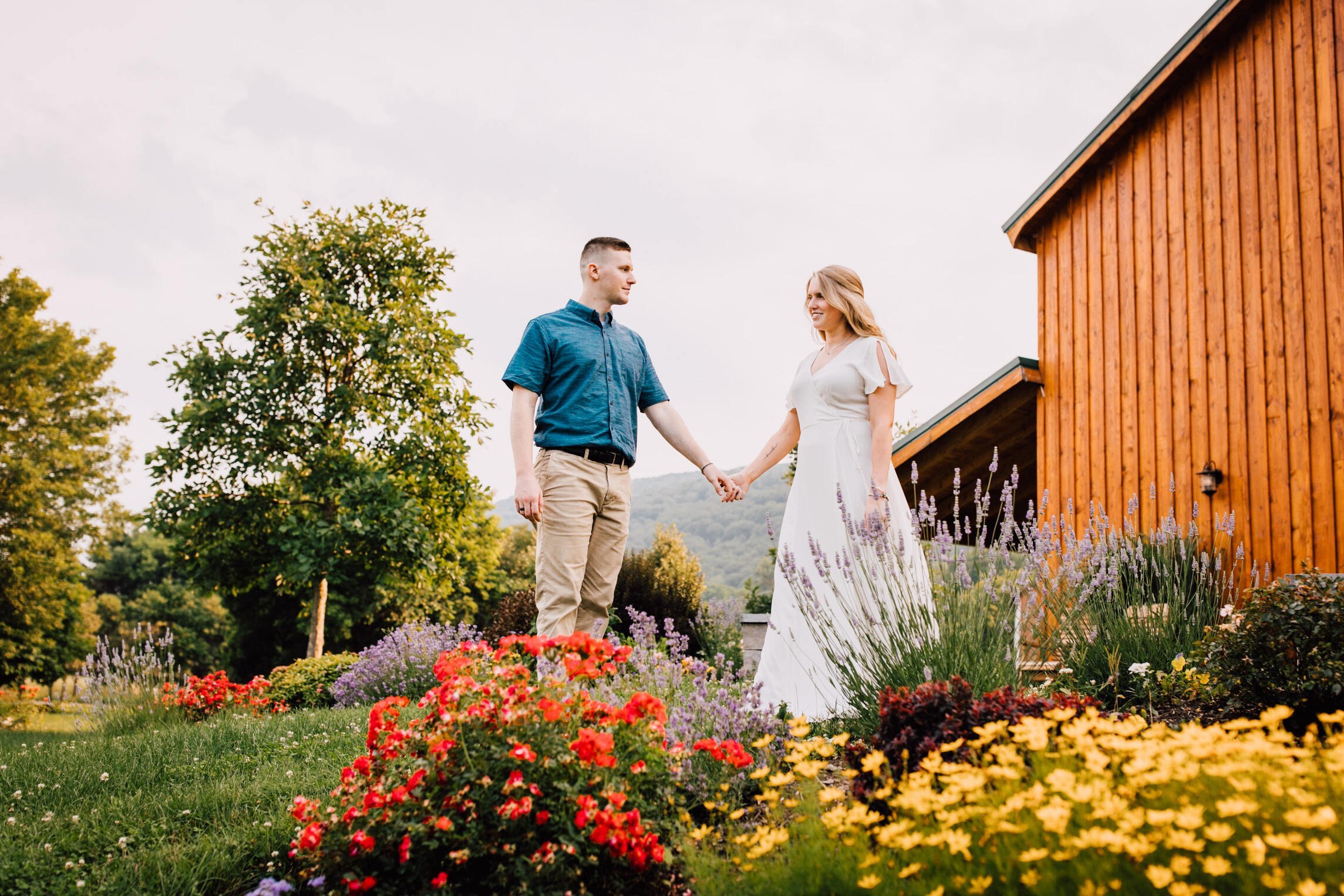  engaged couple stand together while holding hands in front of blooming flowers at rocking horse farm   