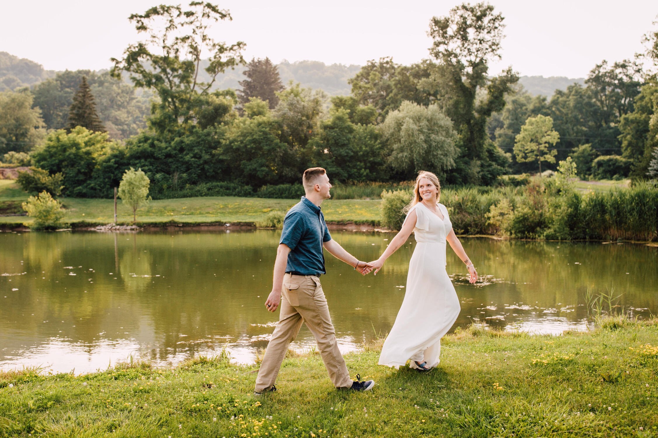 Annie looks back at her fiancé as they walk hand in hand in front of a pond at rocking horse farm 