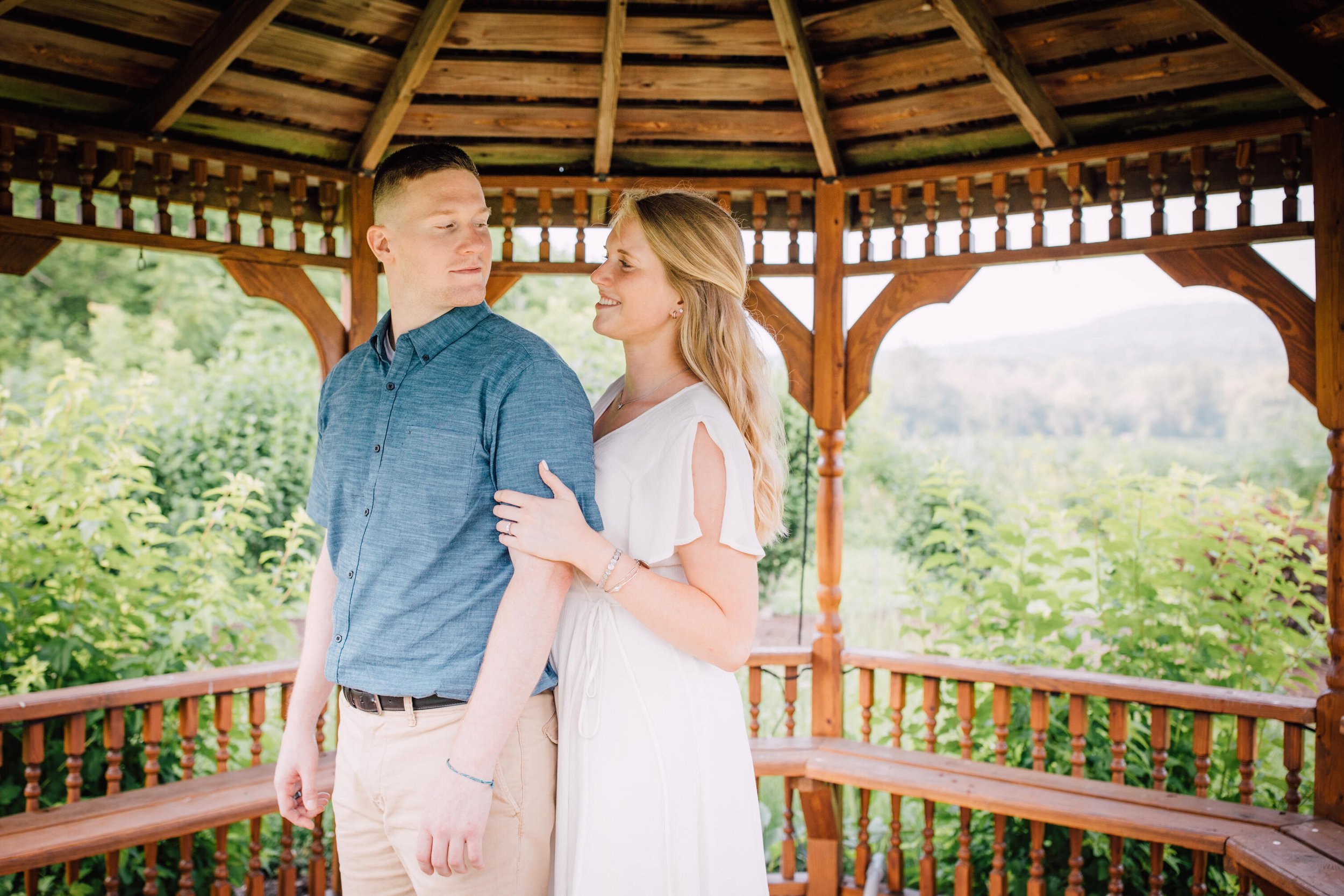  Jake looks back and smiles at his fiancé under a gazebo at rocking horse farm 