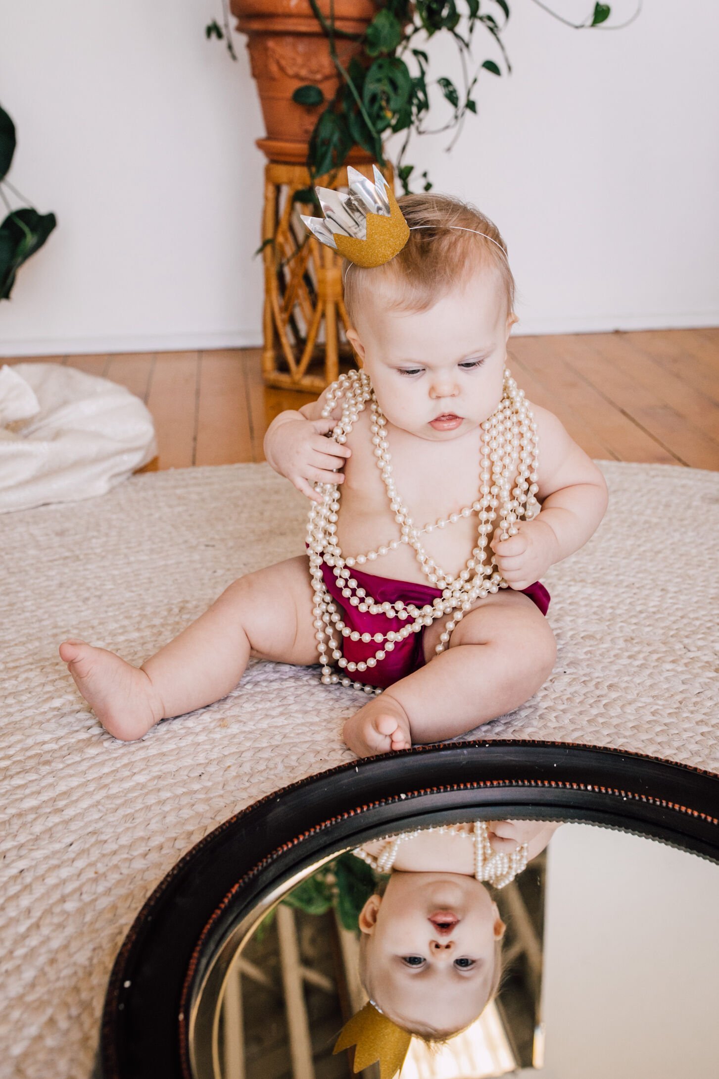  Baby girl wearing pearls and a paper crown looks into a mirror during this moody mommy and me session&nbsp; 