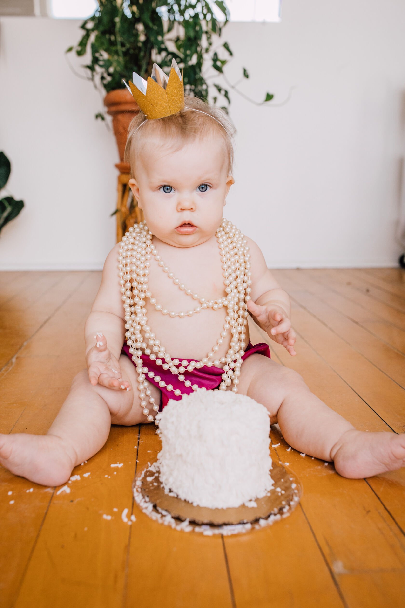  Baby looks at camera while wearing pearls and a paper crown for cake smash photos 