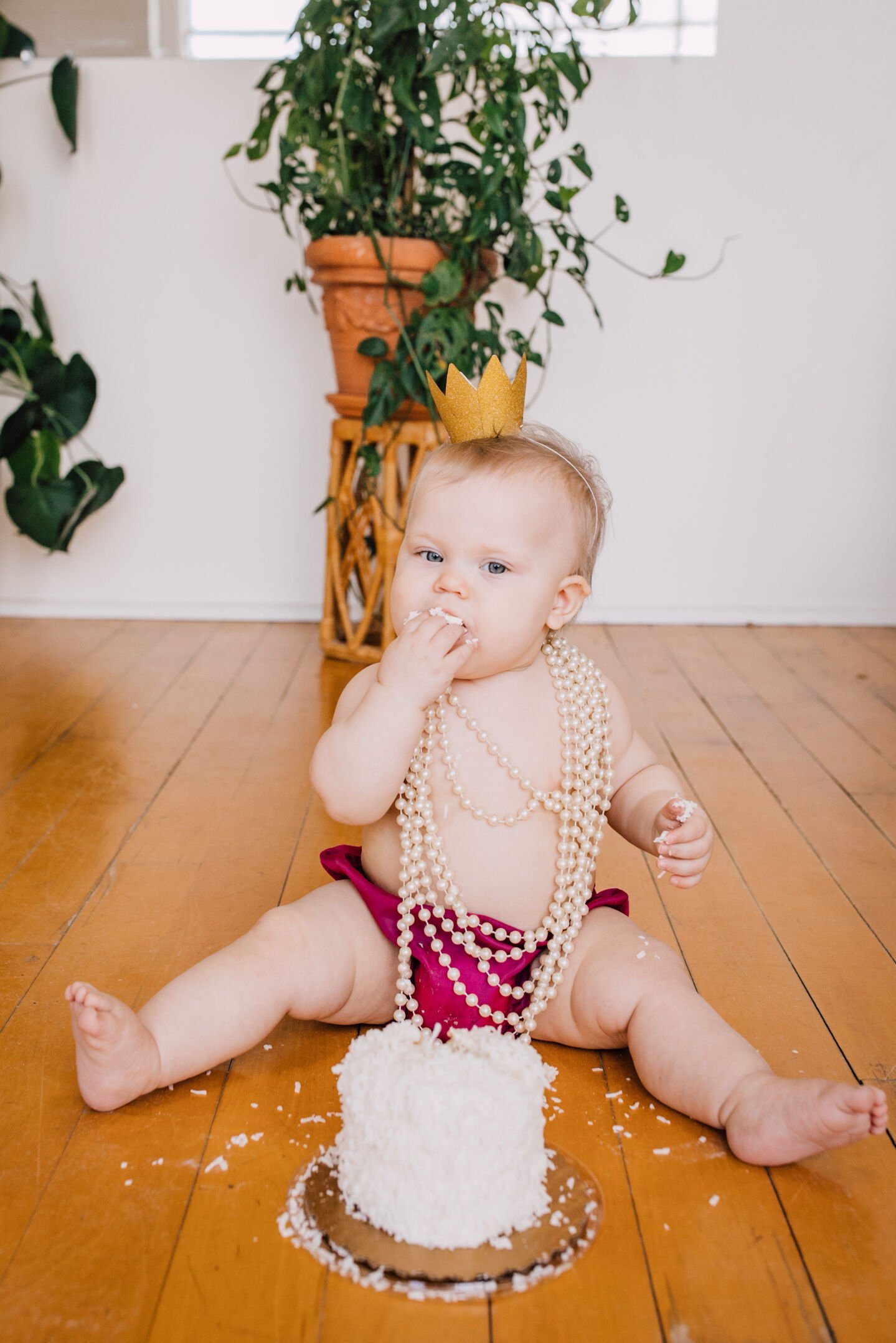  Baby girl wears pearls and a crown during a cake smash session 
