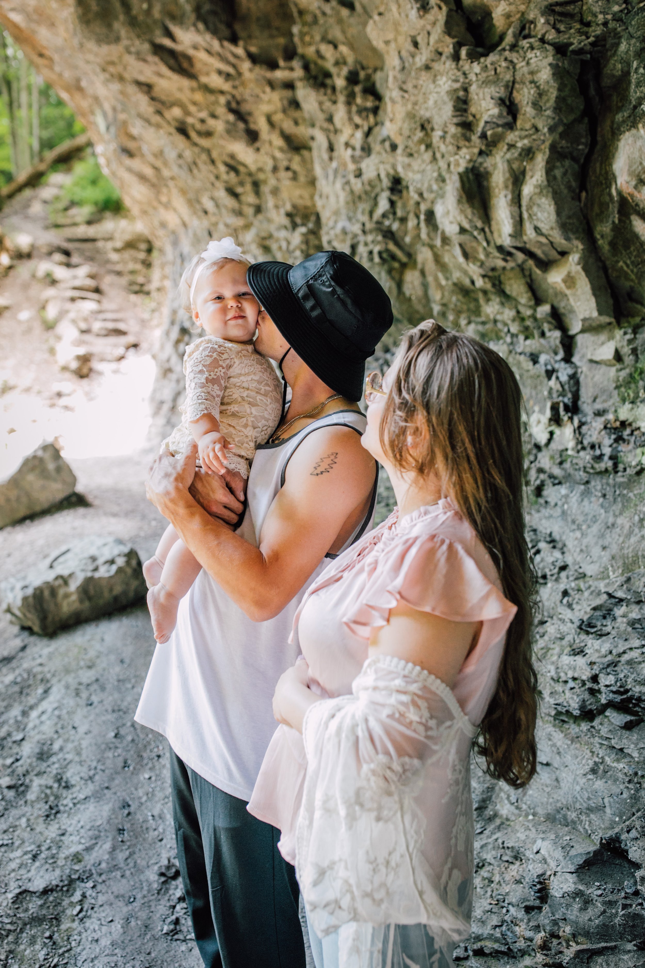  Family stands together in a rocky area while dad kisses their baby’s cheek at a tinker falls waterfall shoot 