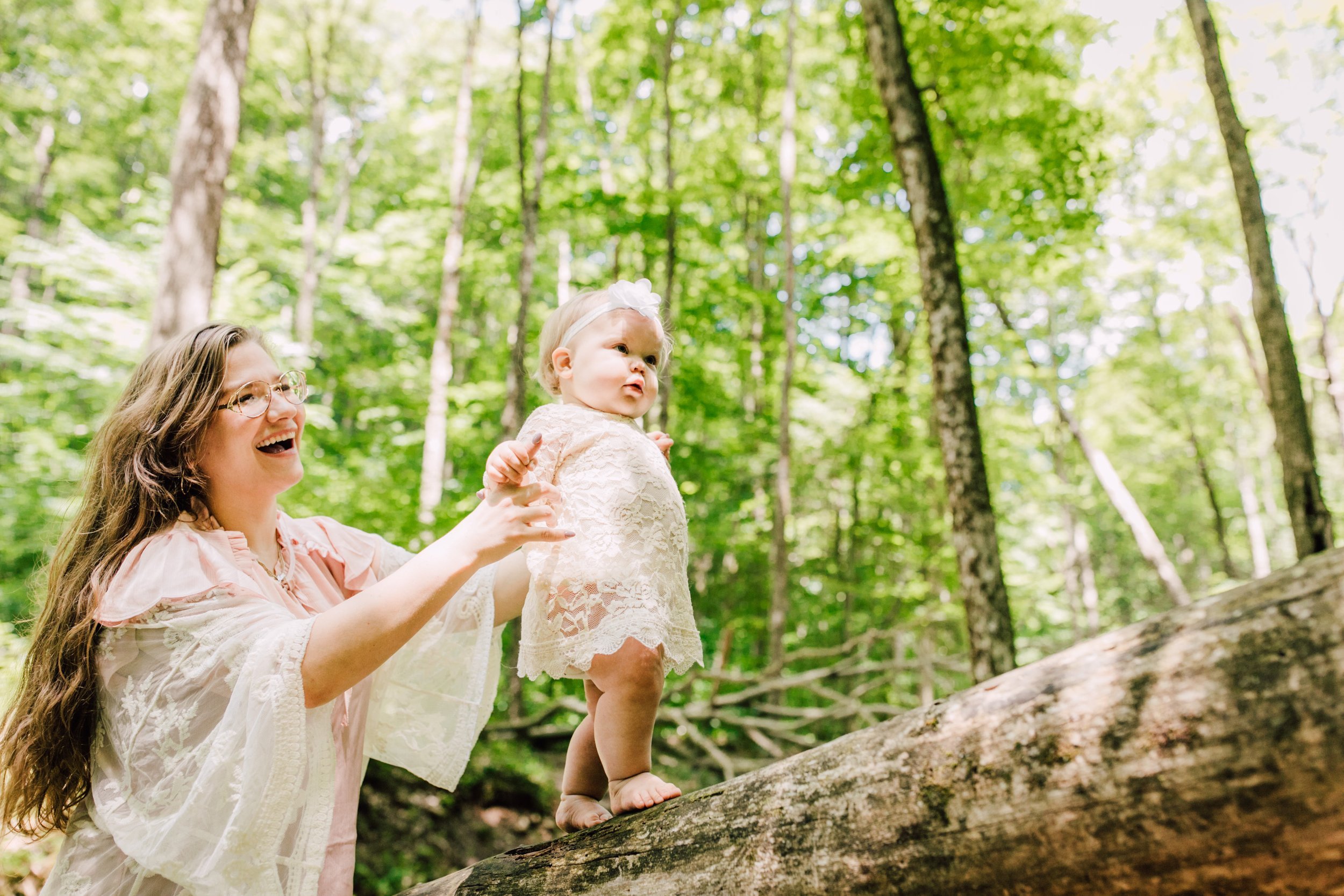  Mama helps her baby girl walk on a fallen tree during a family adventure 