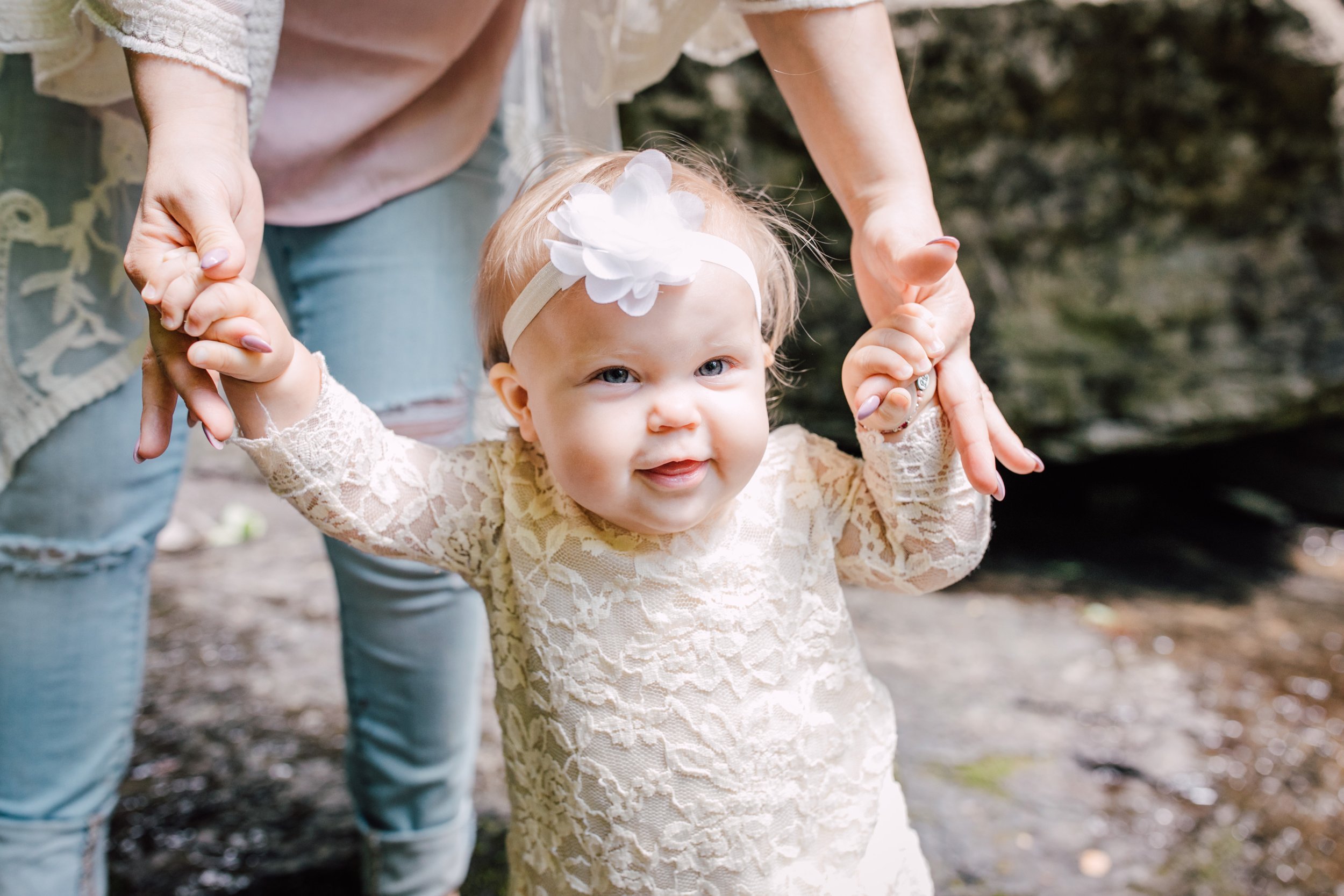  Mom holds her baby’s hands while she smiles during an waterfall photo shoot 