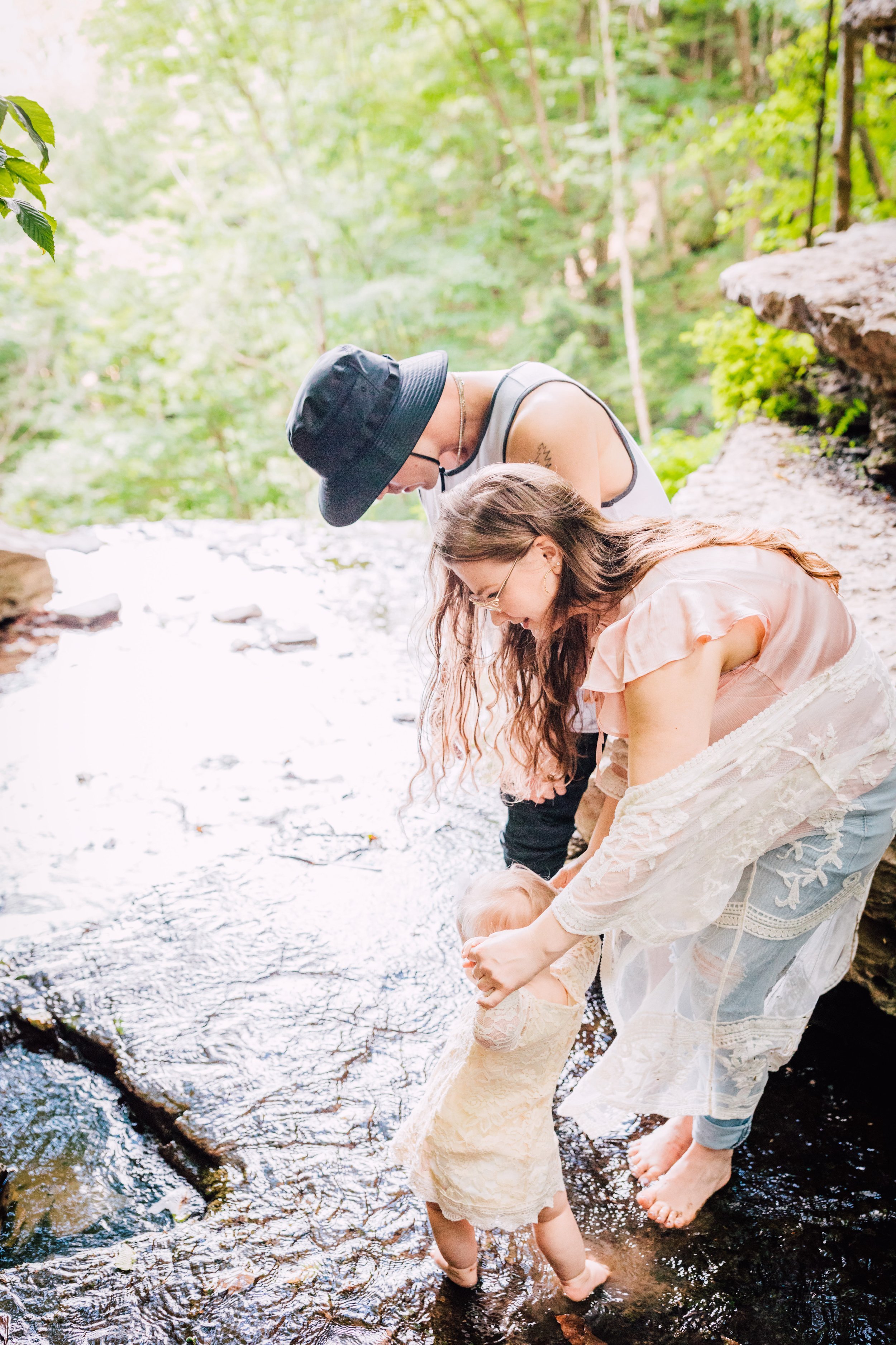  Mom and dad help their baby walk on a stream during a waterfall photo shoot 