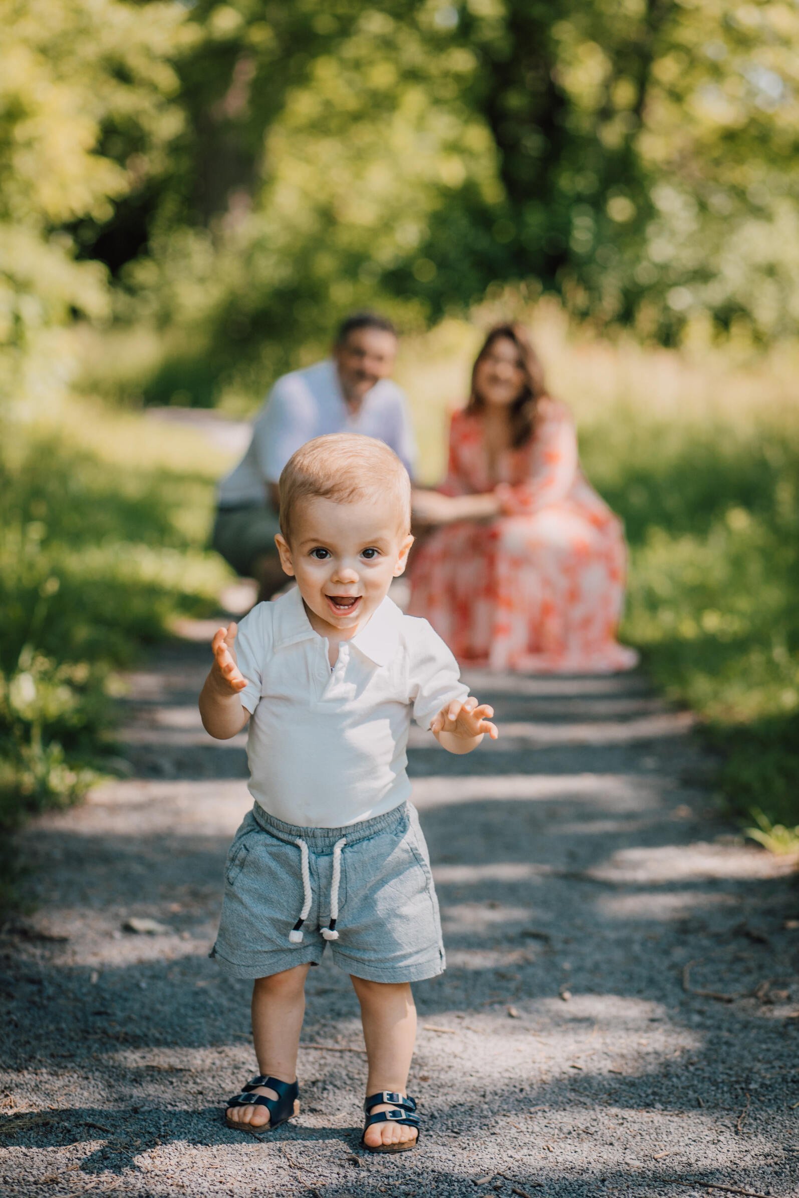  Toddler walks from his parents towards their family photographer&nbsp; 