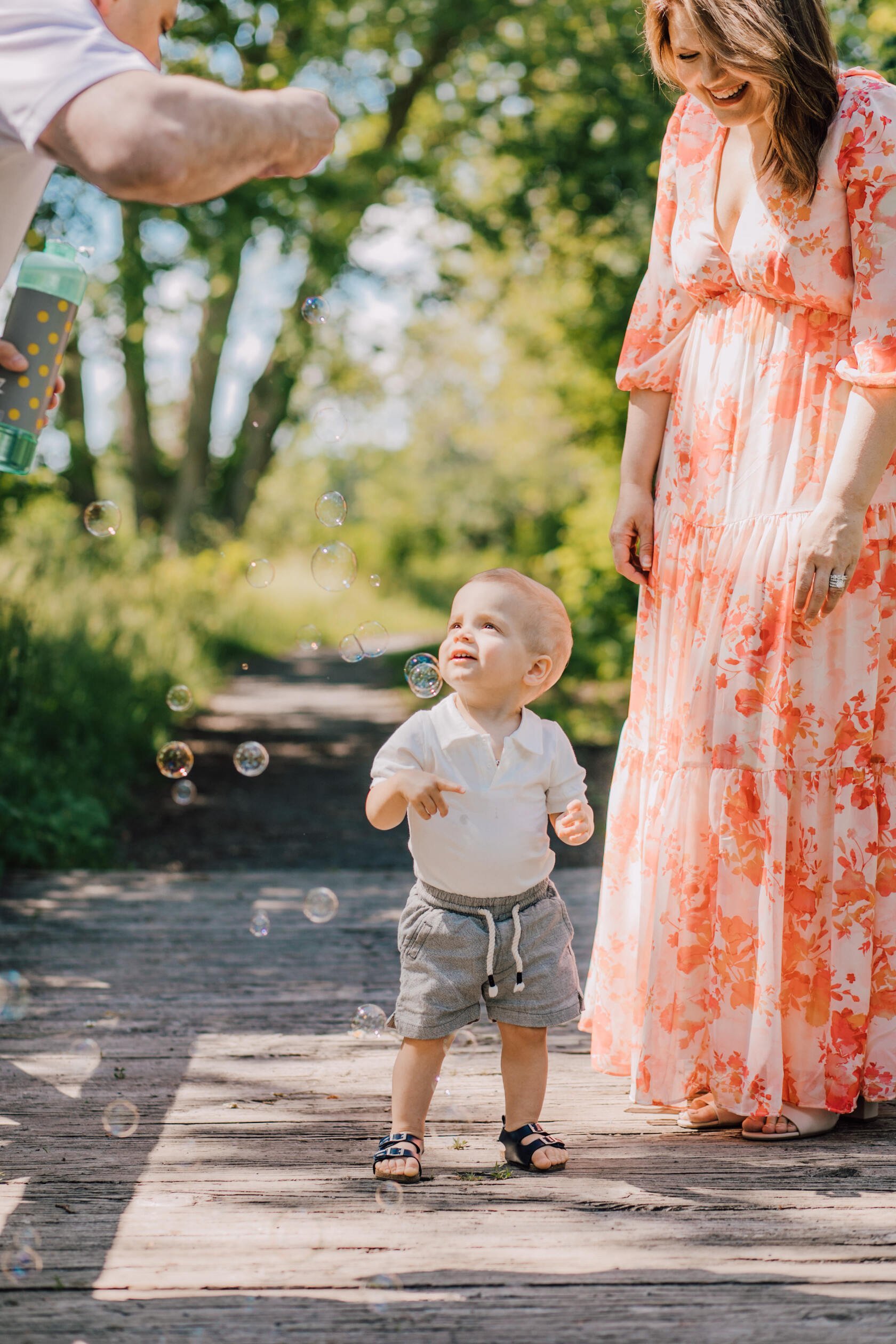  Parents stand with their toddler as he explores bubbles during a family session 
