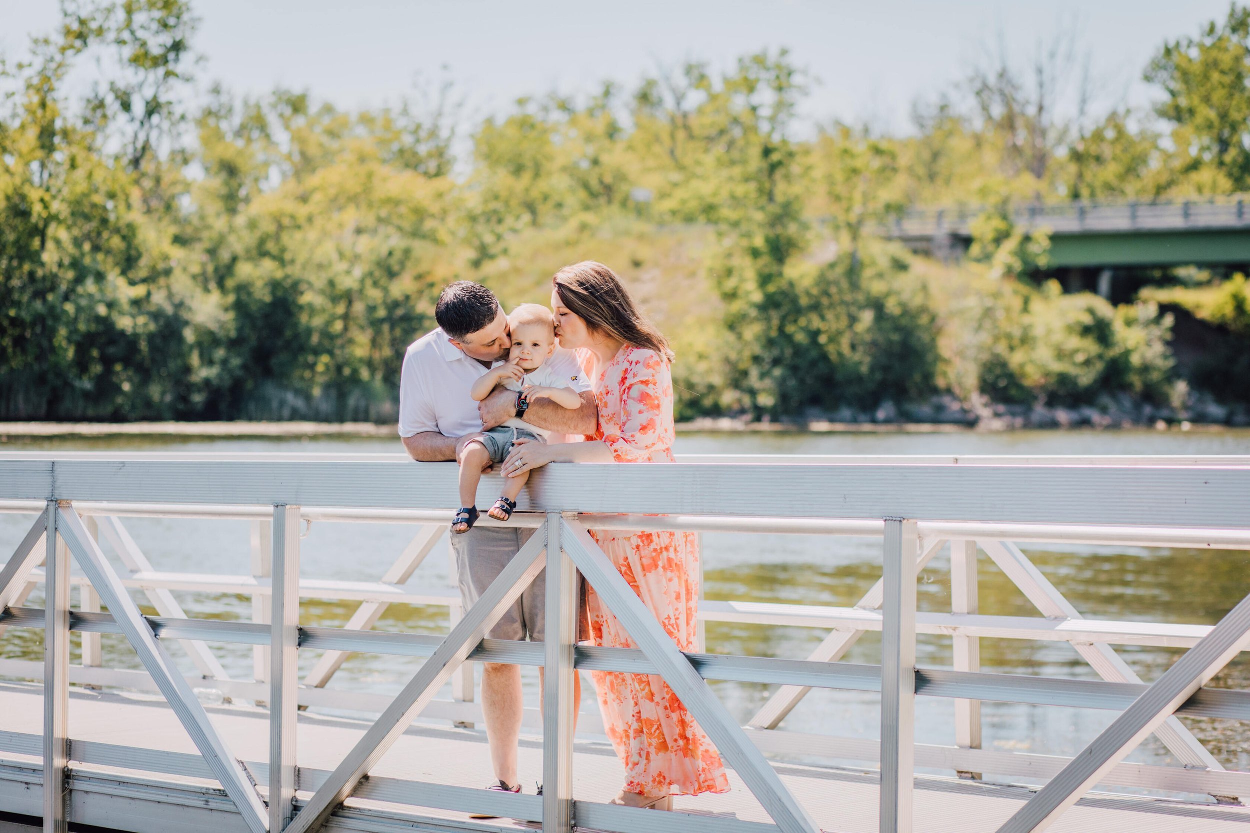  Family photographer captures parents kissing their toddler on the head on a bridge at Onondaga Lake 