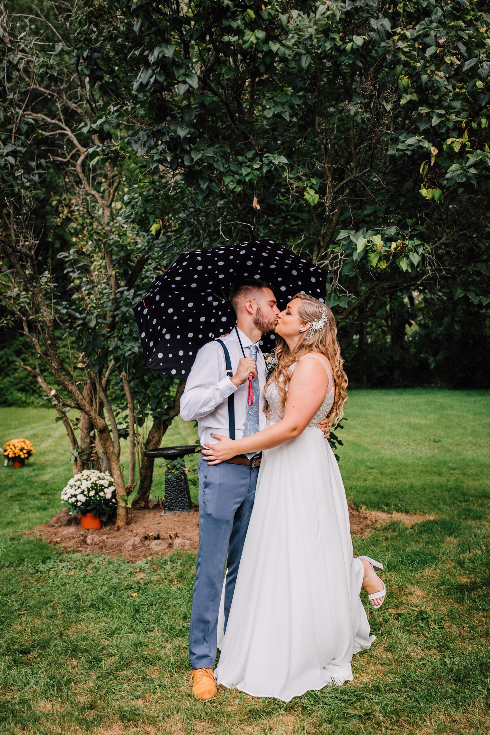  Bride and groom kiss under an umbrella in the rain before their backyard wedding reception 