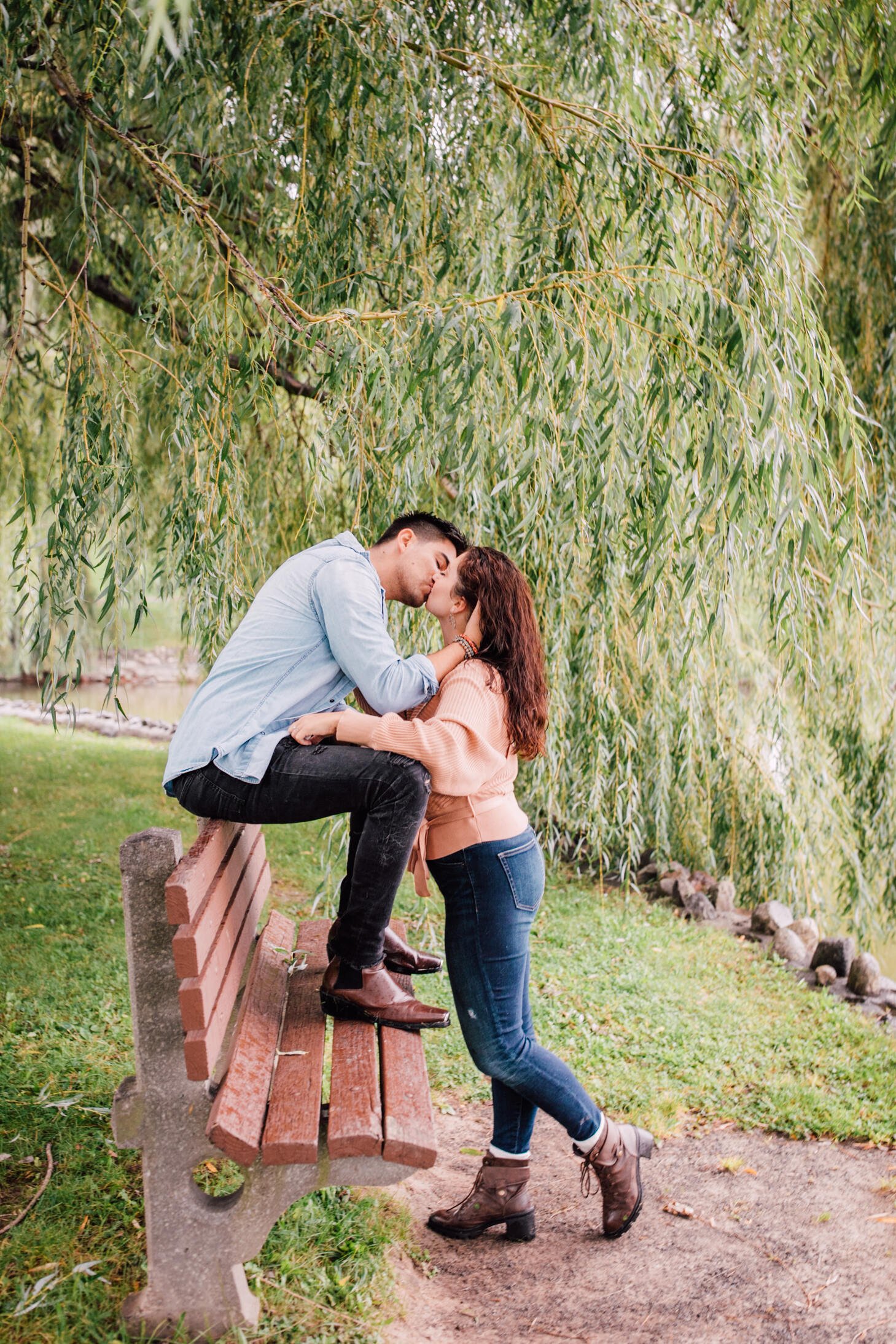  jessica and pablo share a kiss on a park bench under a willow tree during their rainy engagement photos 