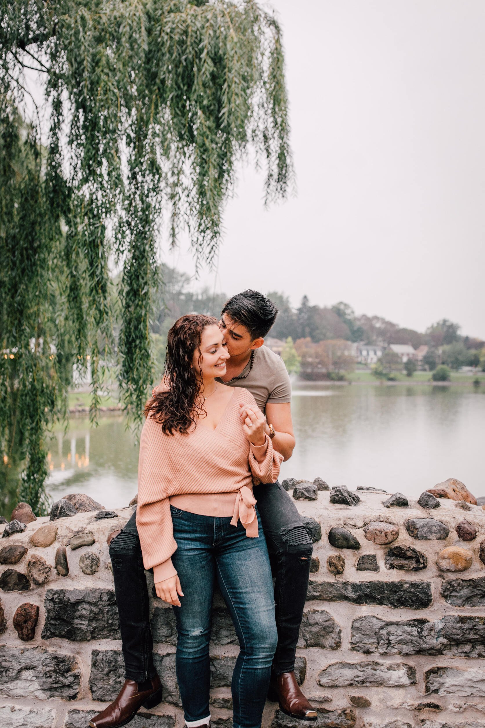  pablo kisses jessica’s cheek as they lean against a rock bridge during their romantic engagement photos 
