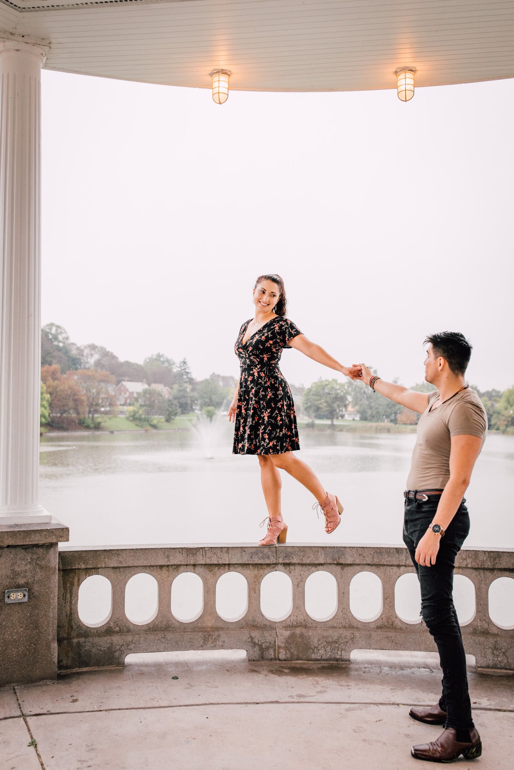  jessica looks back at pablo as he holds her hand while she stands on a railing while their romantic engagement photos are taken  