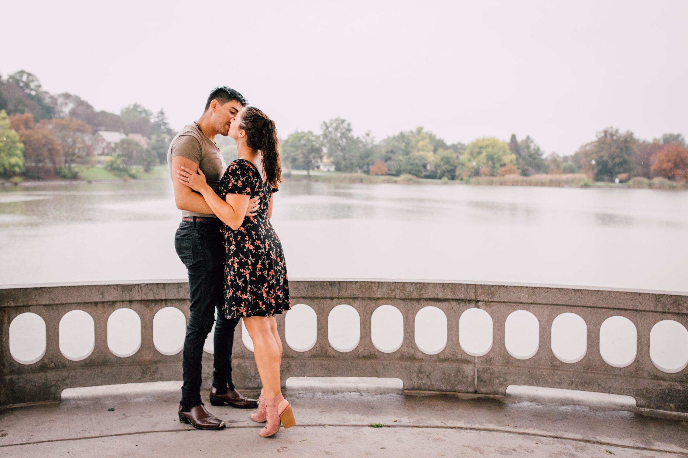  jessica leans into pablo on her tip toes as they kiss under a gazebo that sits in front of a lake during their engagement photos in the rain 