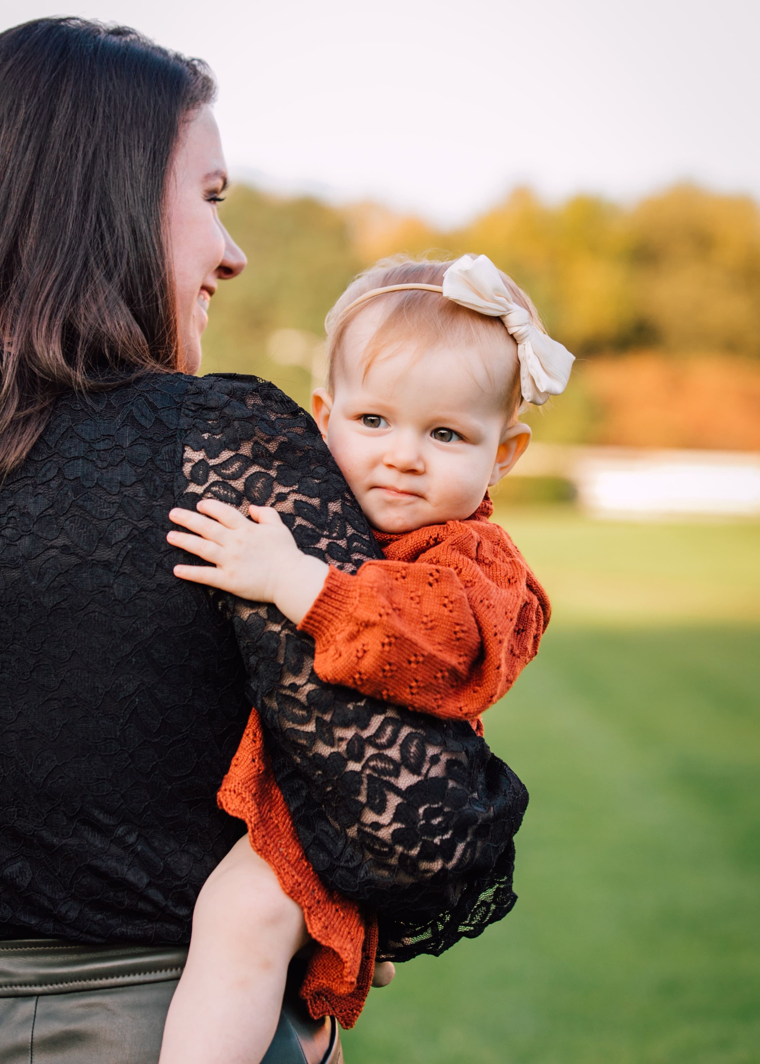  mom smiles as she holds baby girl who smiles while wearing an orange sweater dress for fall family photos 
