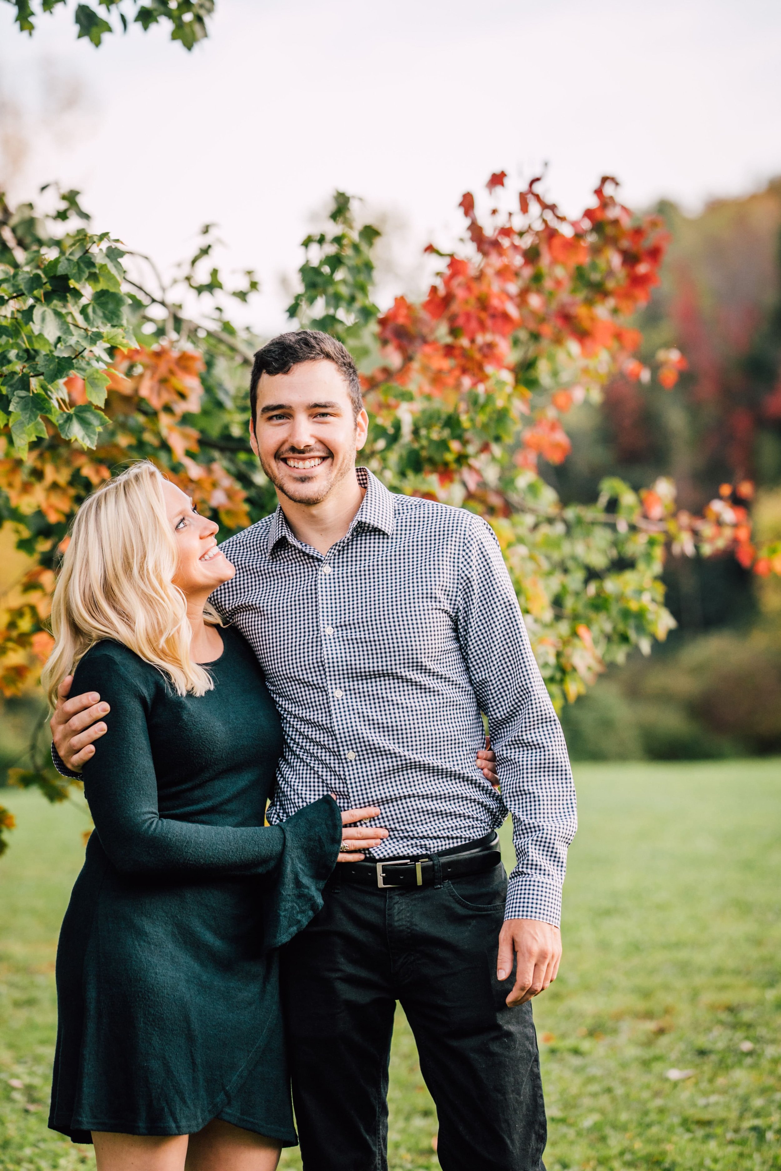  woman smiles up at her fiancee as he smiles with his arm around her shoulders during adult family photos 