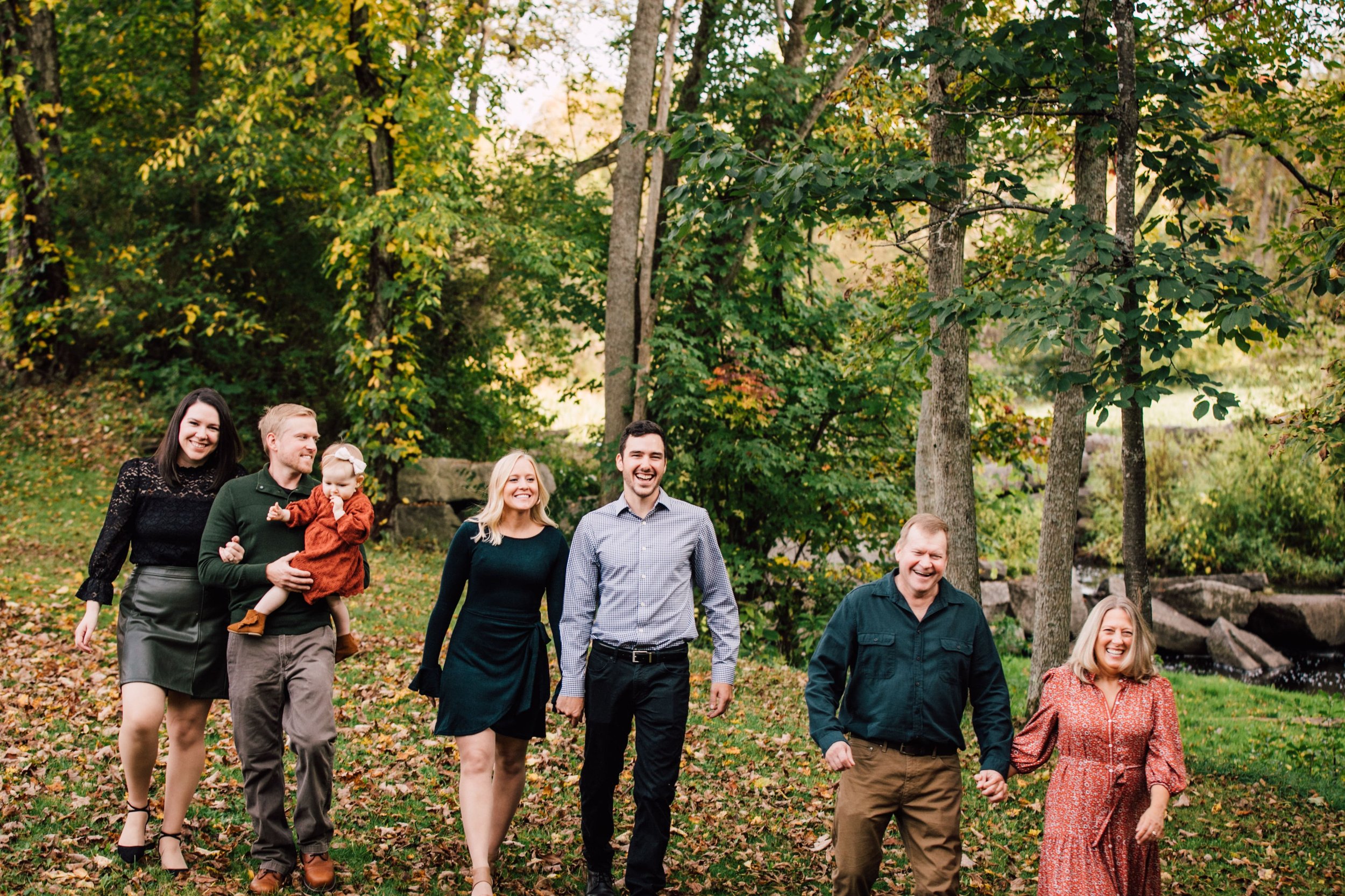  a cinematic photo of a family of 7 walking together while smiling in a wooded area as the colors change for fall family photos 