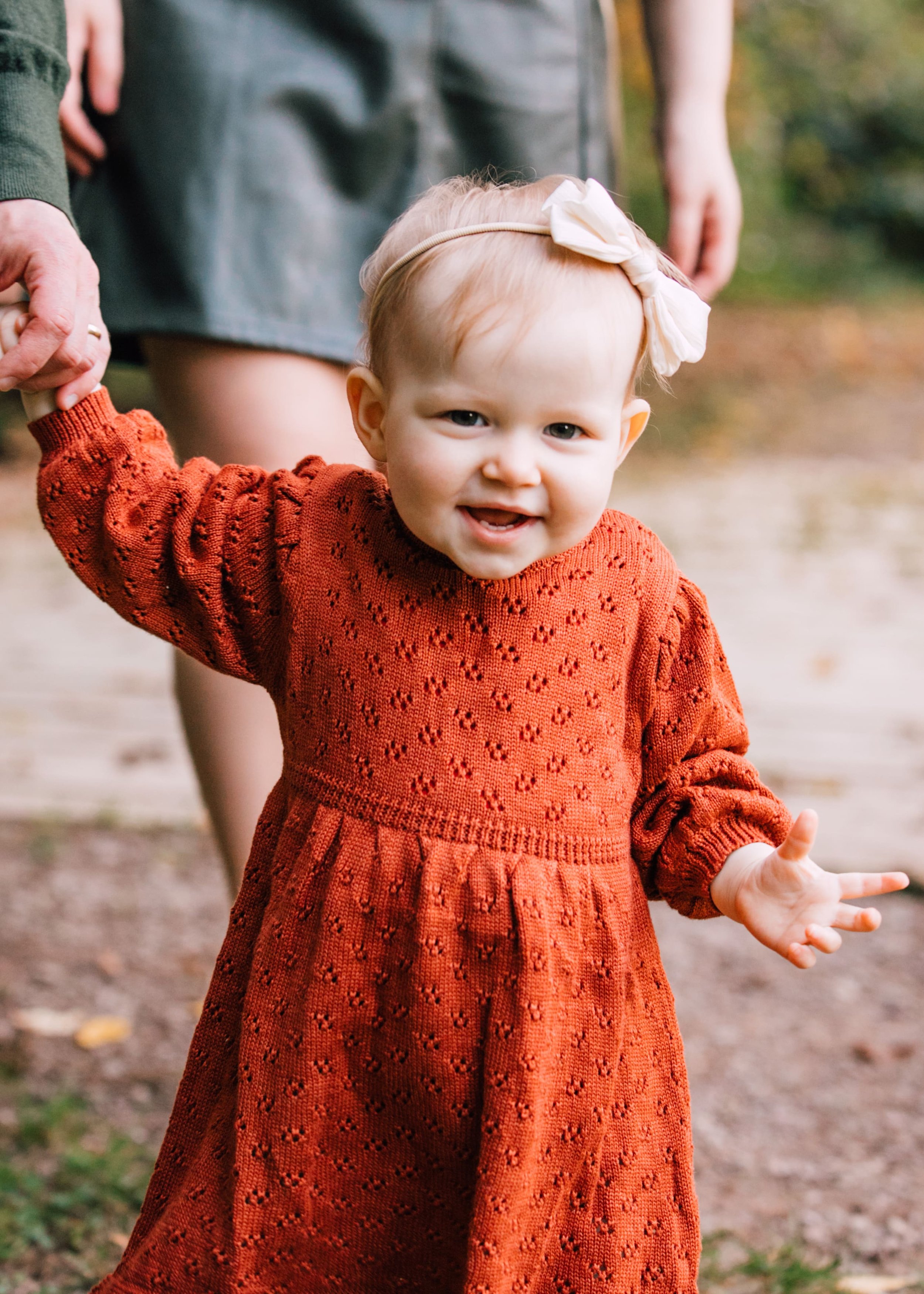  a baby smiles as she walks with her parents during family photos in Oswego, NY 