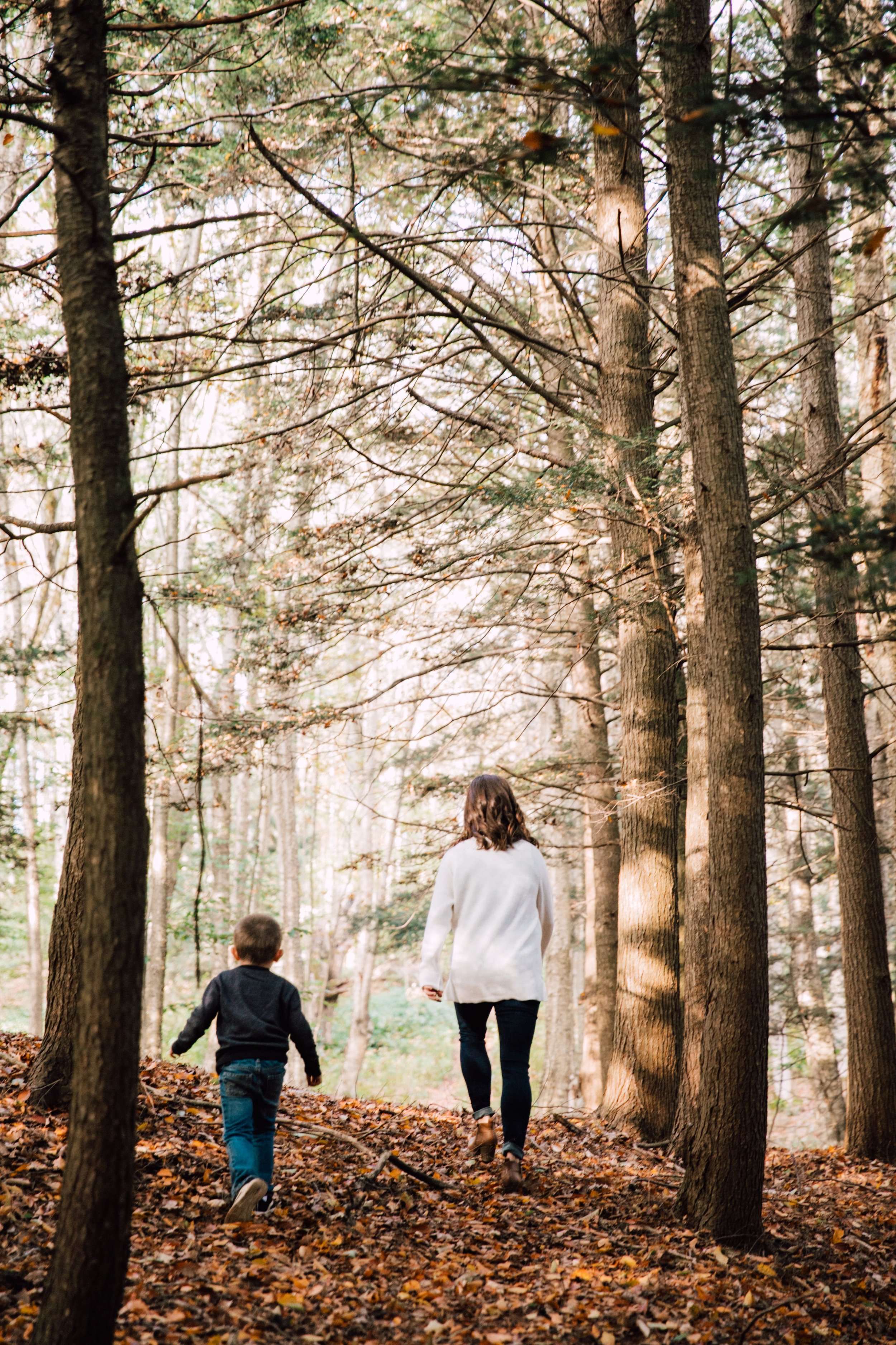 megan walks through a wooded area with her son in tow during their backyard photoshoot 